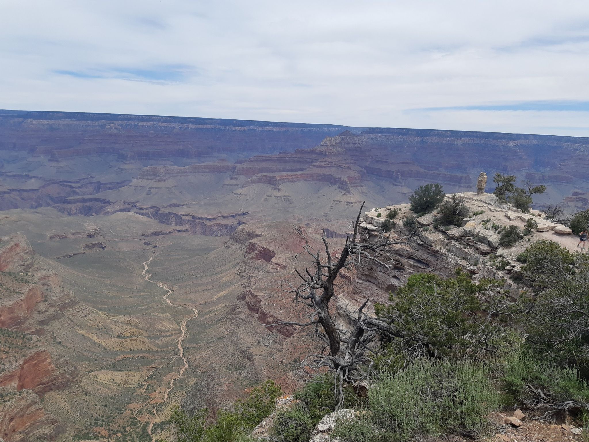 Wide canyon view with a distant monument on a rocky outcrop under cloudy sky. - Shoshone Point Trail