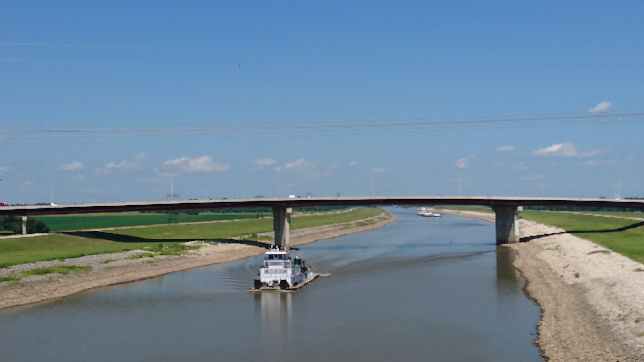 A white boat navigates a wide canal under a concrete bridge. - Mississippi River Trail: St. Louis Loop