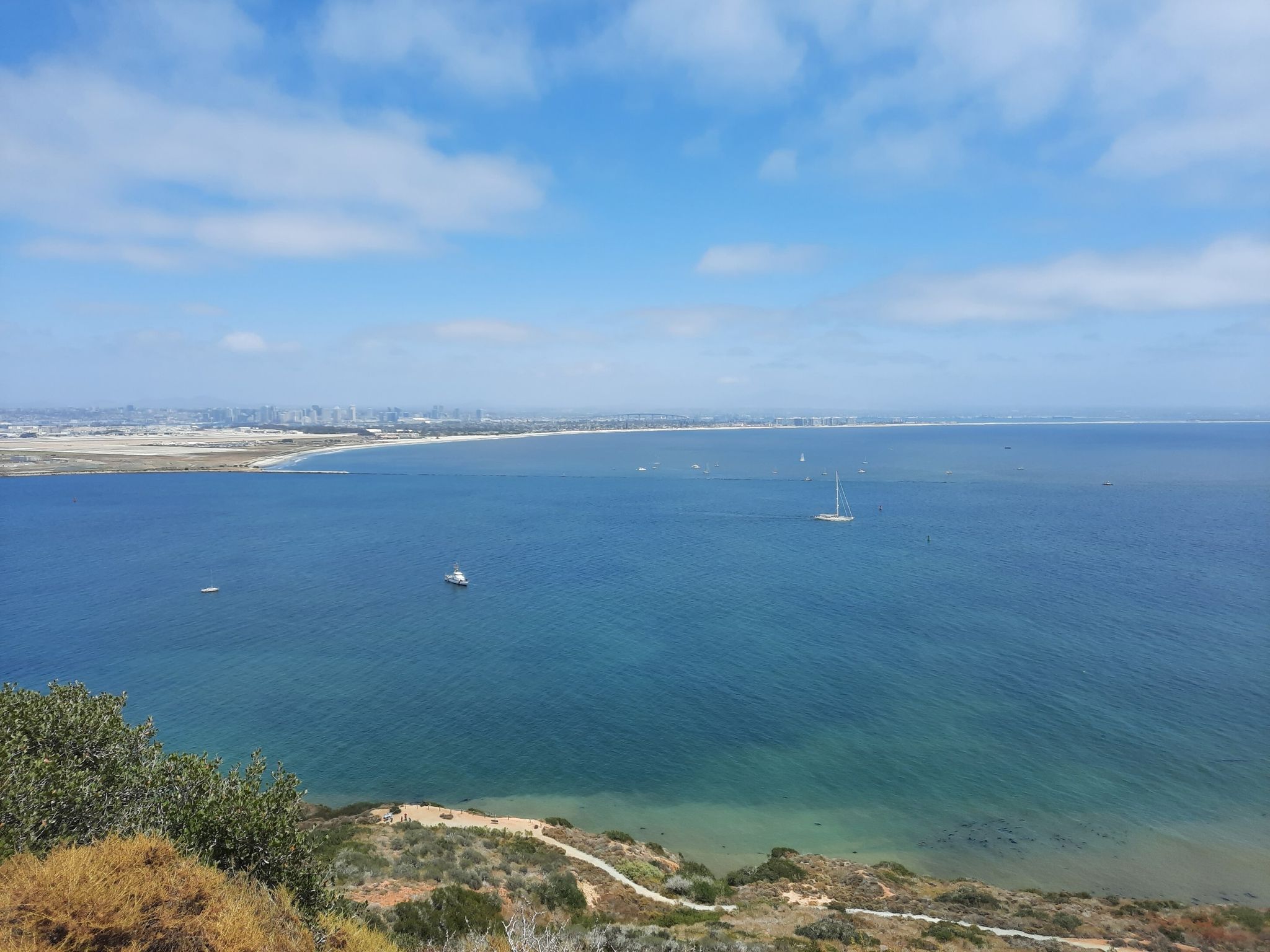 Bright day overlooking a wide bay with boats and a distant city. - Bayside Trail