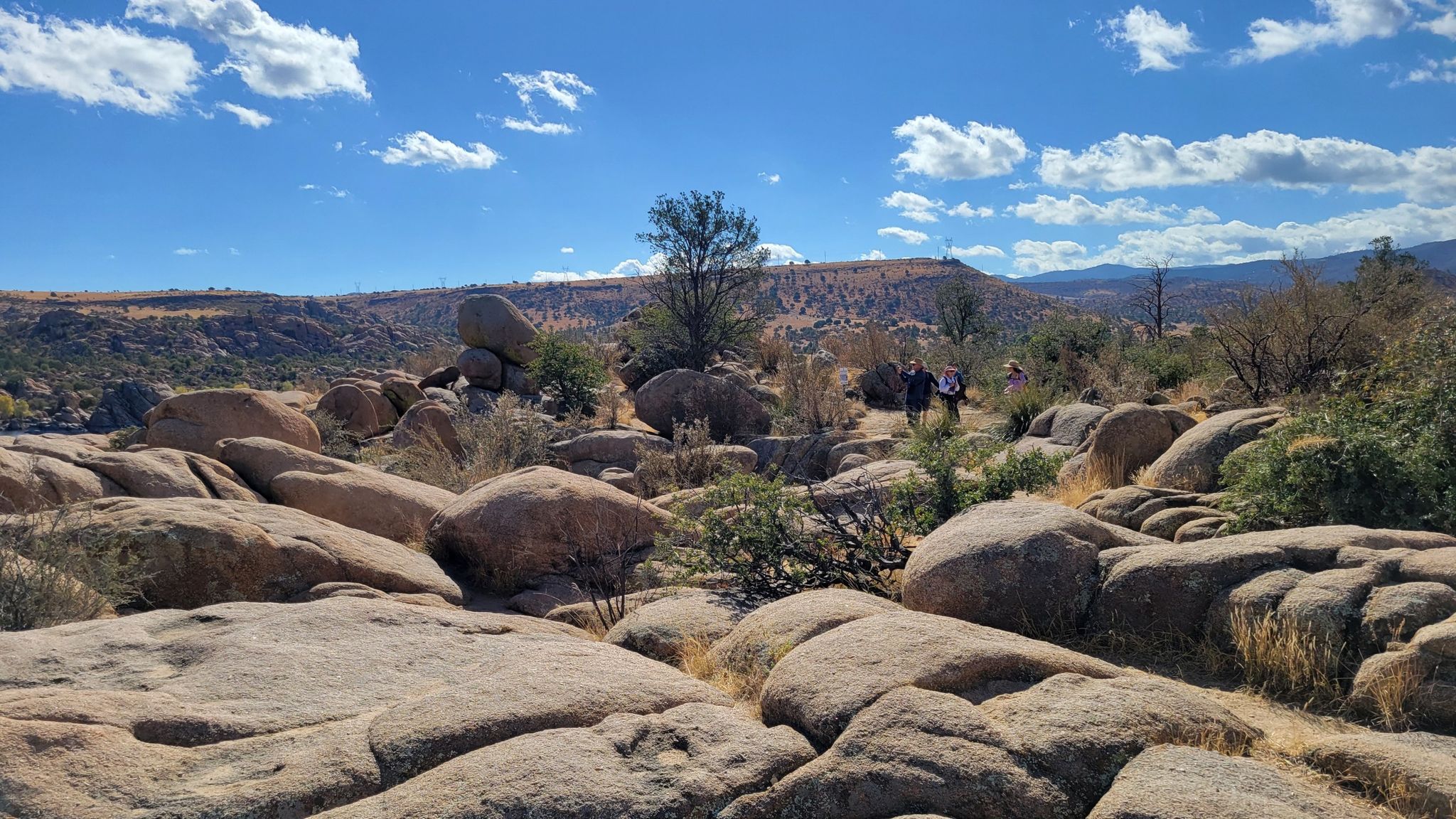 Group of people hiking among large boulders under a partly cloudy sky. - Peavine and Iron King Trail Loop