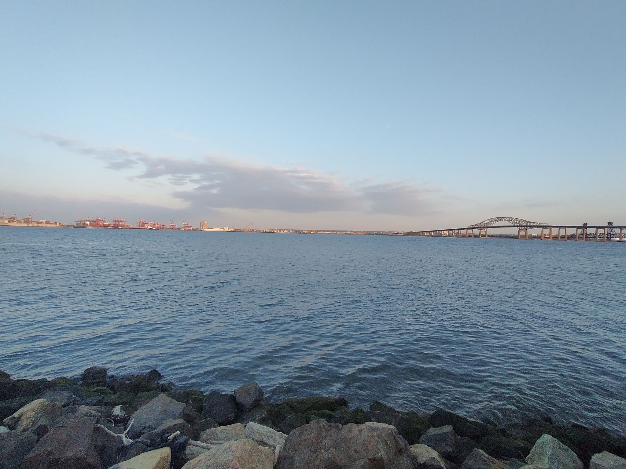 Wide expanse of blue water with a rocky shore and distant bridge. - Stephen R. Gregg Park loop from Marist High School