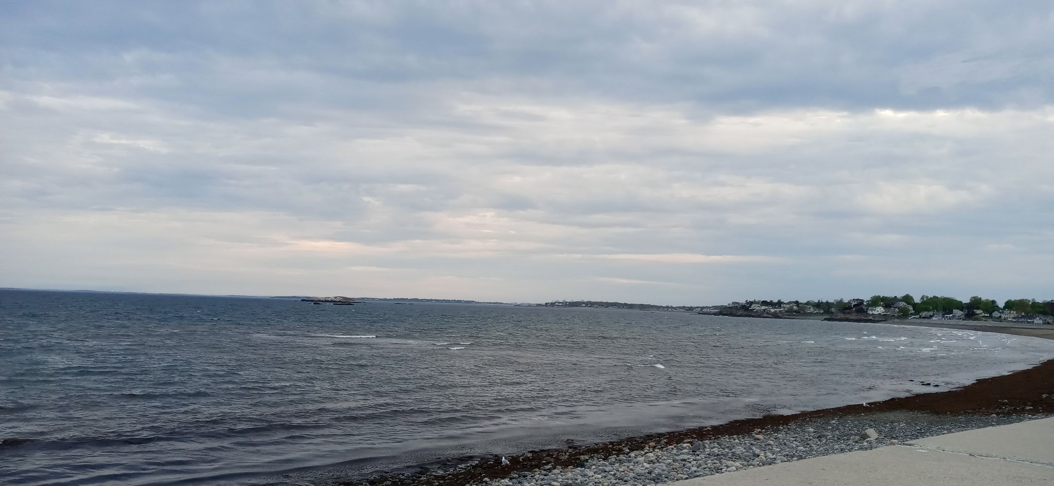 Wide ocean view with a rocky shore and distant town under cloudy skies. - Marblehead & Winter Island loop from Beverly