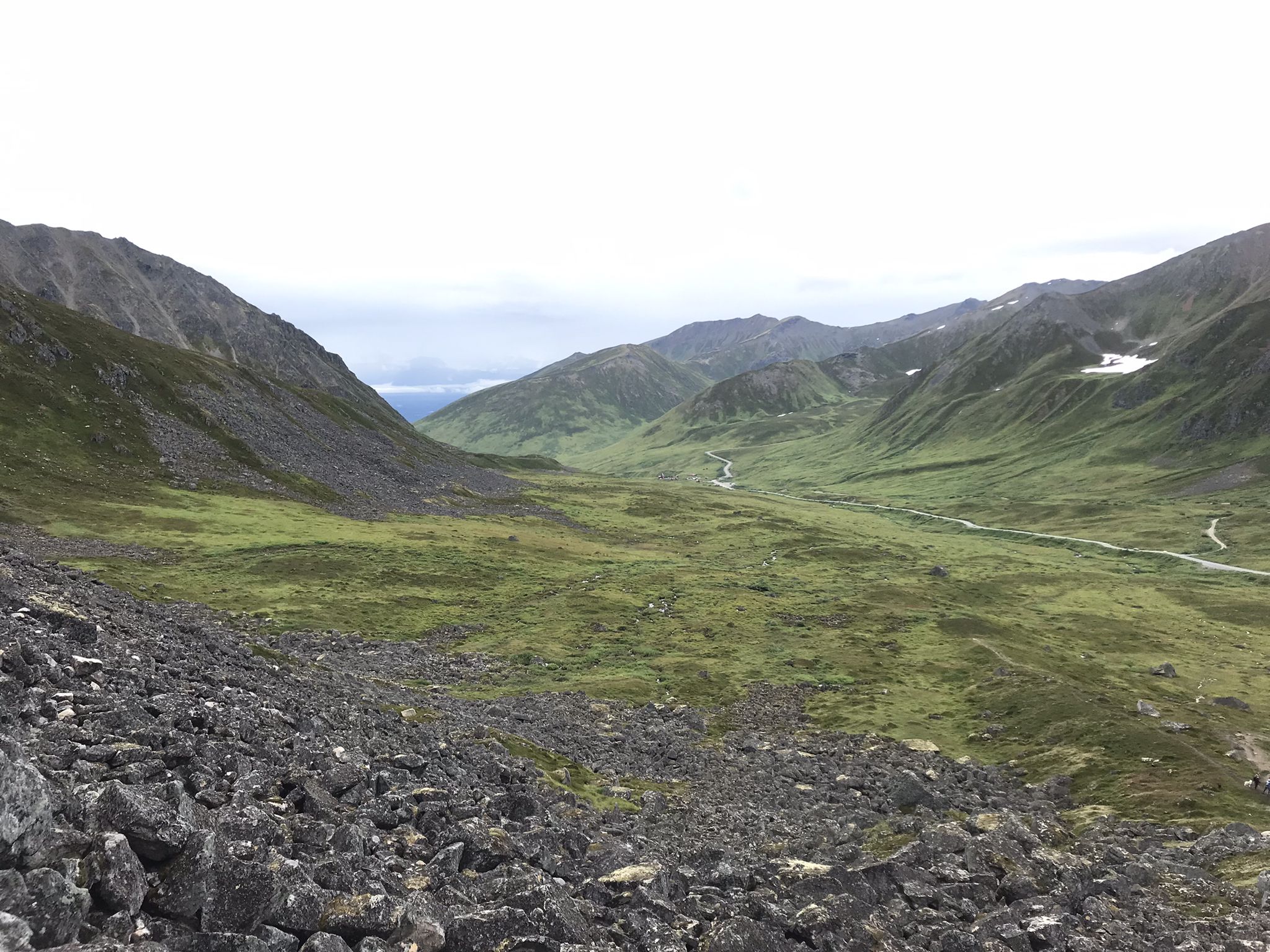Expansive green mountain valley with rocky foreground under a cloudy sky. - Gold Cord Lake Trail