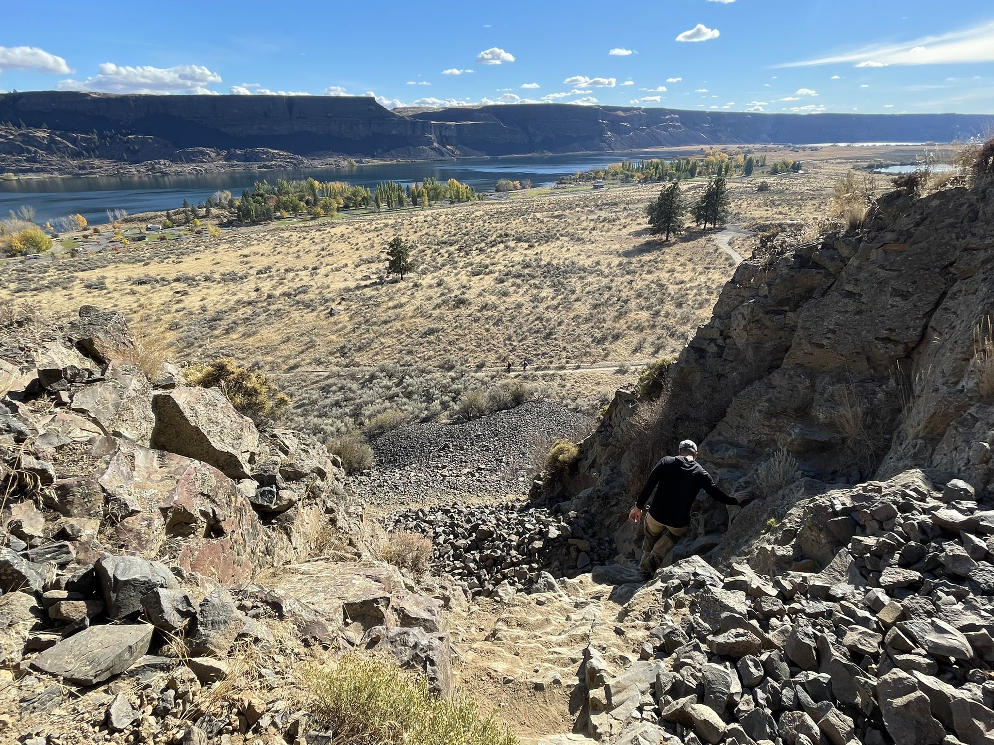 Person carefully descends a steep, rocky path overlooking a sunny valley and lake. - Viewpoint – Steamboat Rock Trail loop from Steamboat Rock State Park Campground