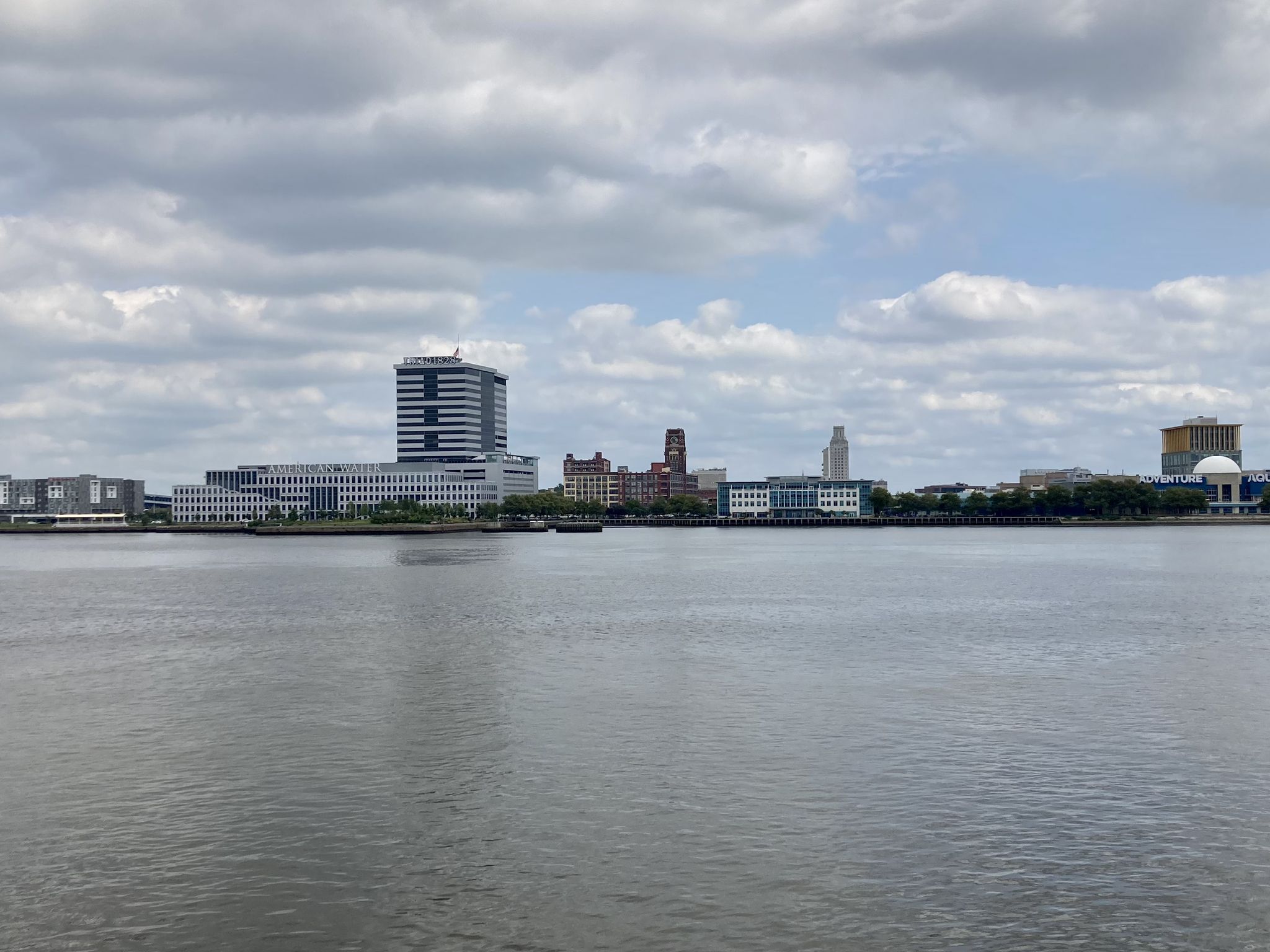 City skyline with modern and older buildings across a wide river under cloudy sky. - Great Plaza at Penn's Landing – Race Street Pier loop from Independence Hall World Heritage Site