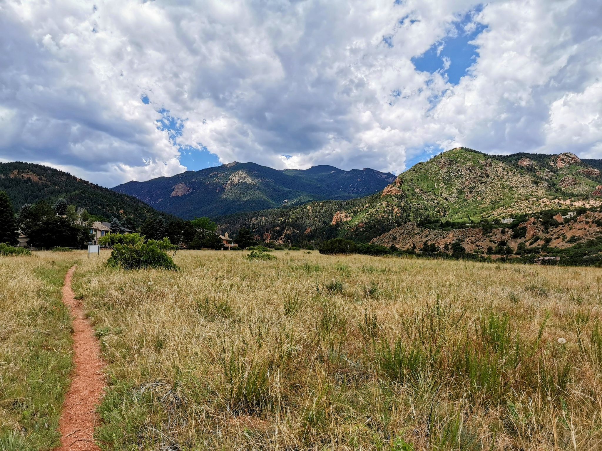 A dirt path through a golden grassy field leads to distant mountains under a cloudy sky. - Coyote Gulch Loop