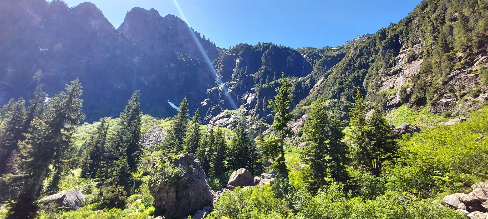 Sunny mountain valley with steep, forested slopes and green trees. - Heather Lake Trail