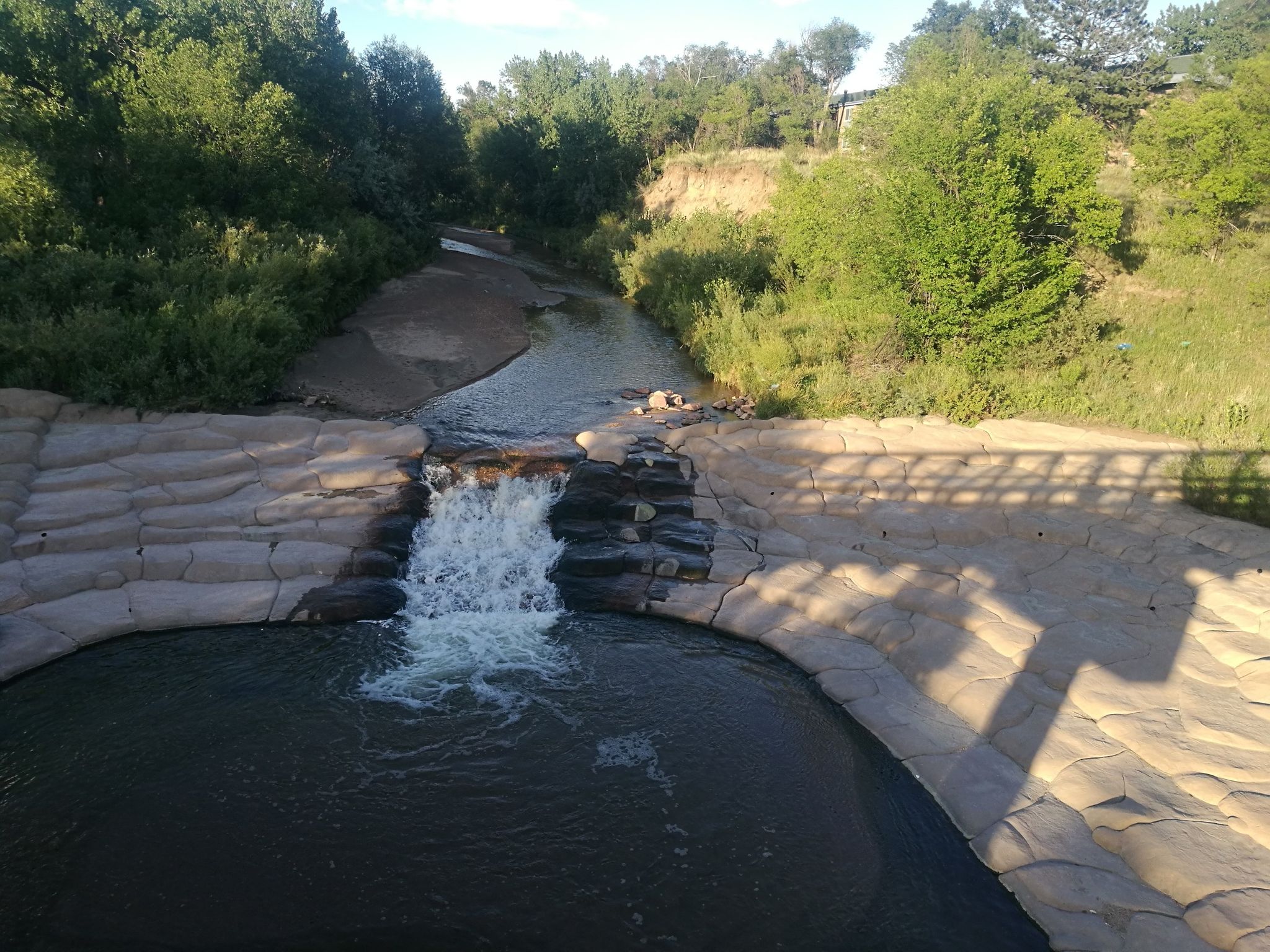 Small waterfall over textured rock into a river, surrounded by trees. - North Cascade to Pikes Peak Greenway loop