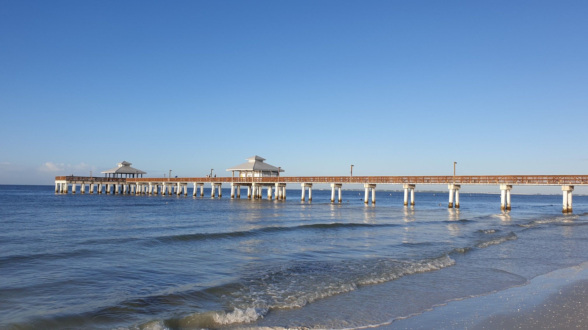 Long pier with two shelters stretching over the ocean under a clear blue sky. - Fort Myers Fishing Pier loop from Fort Myers Beach
