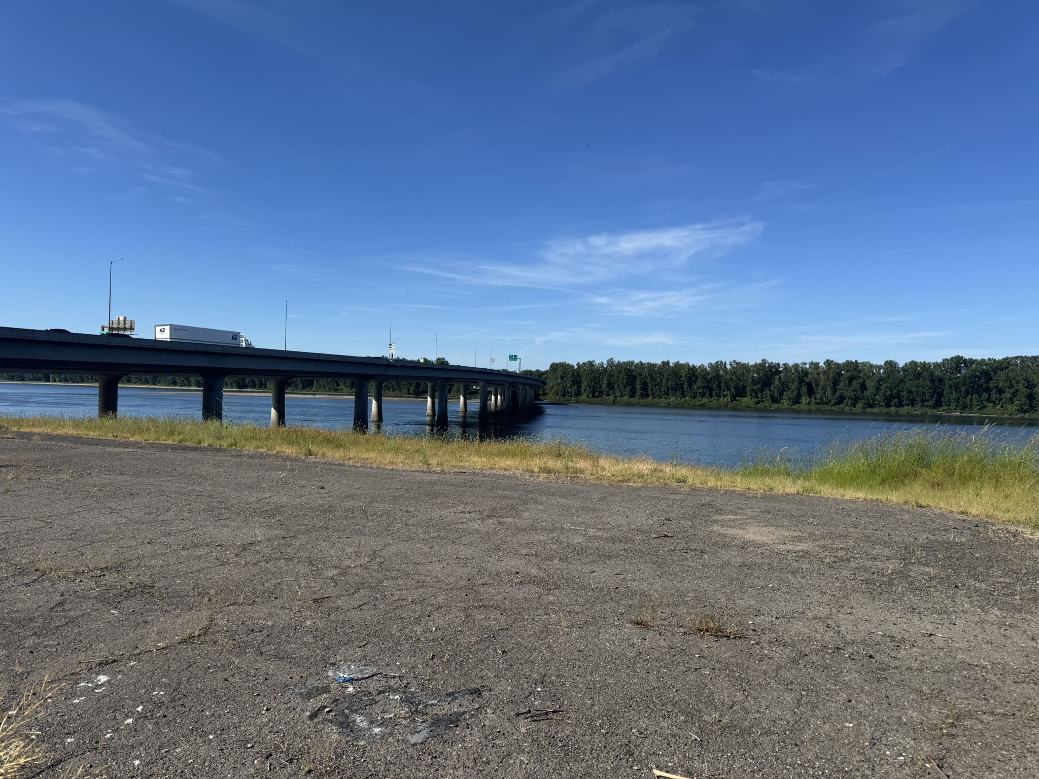 Paved area next to a river with a long bridge and distant trees. - Bike loop from Mountain View High School