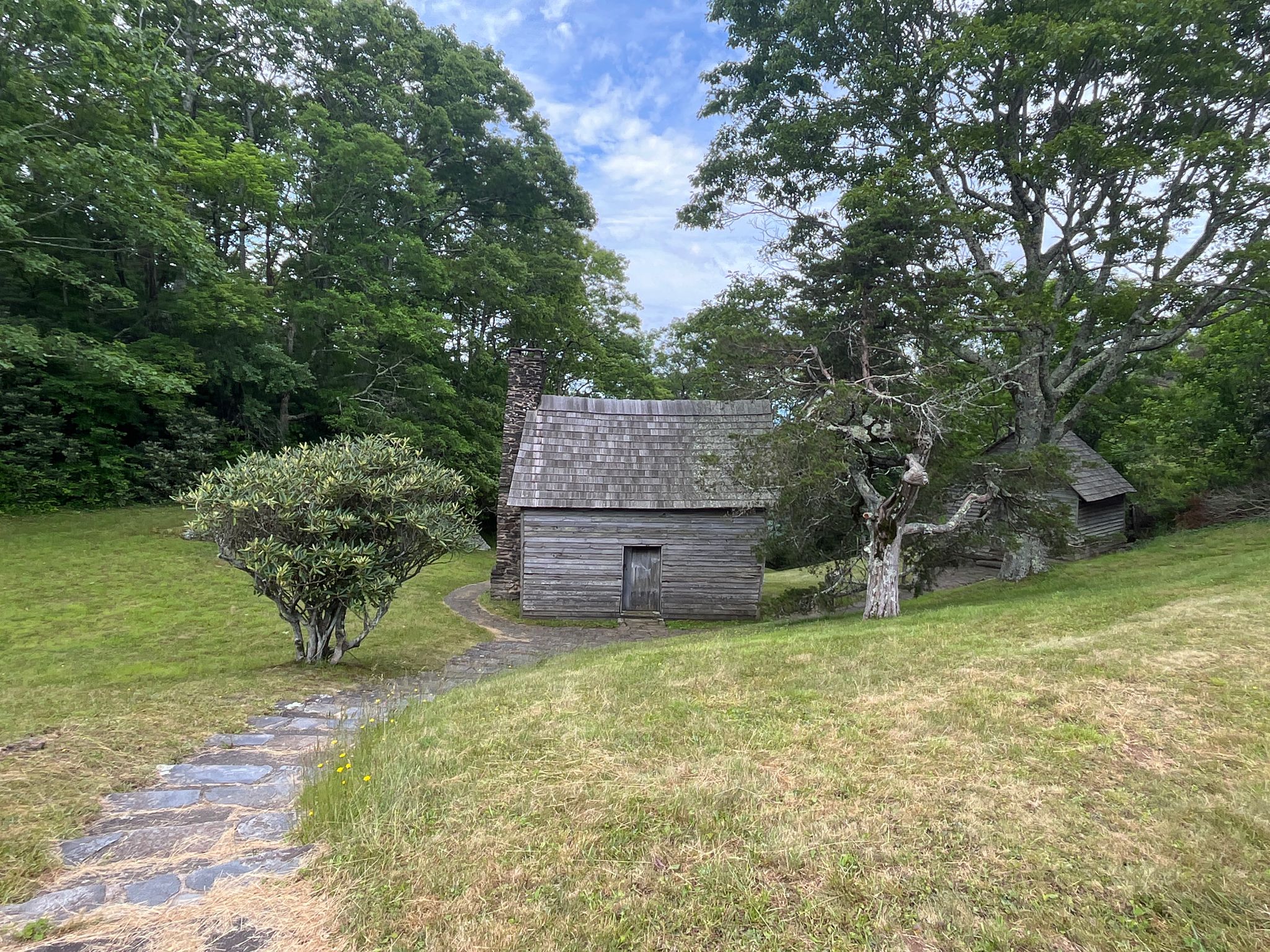 An old wooden cabin with a stone chimney sits on a grassy hill. - Cedar Ridge Trail
