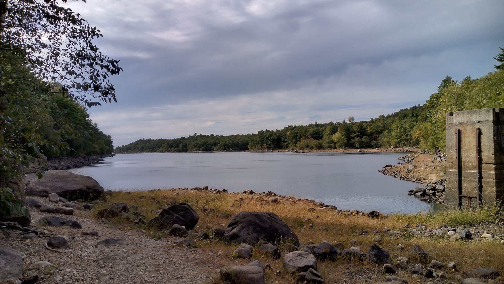 Overcast view of a lake with rocky shores and a concrete structure. - Lynn Woods Reservation Loop South (long) – Lynn Woods Reservation