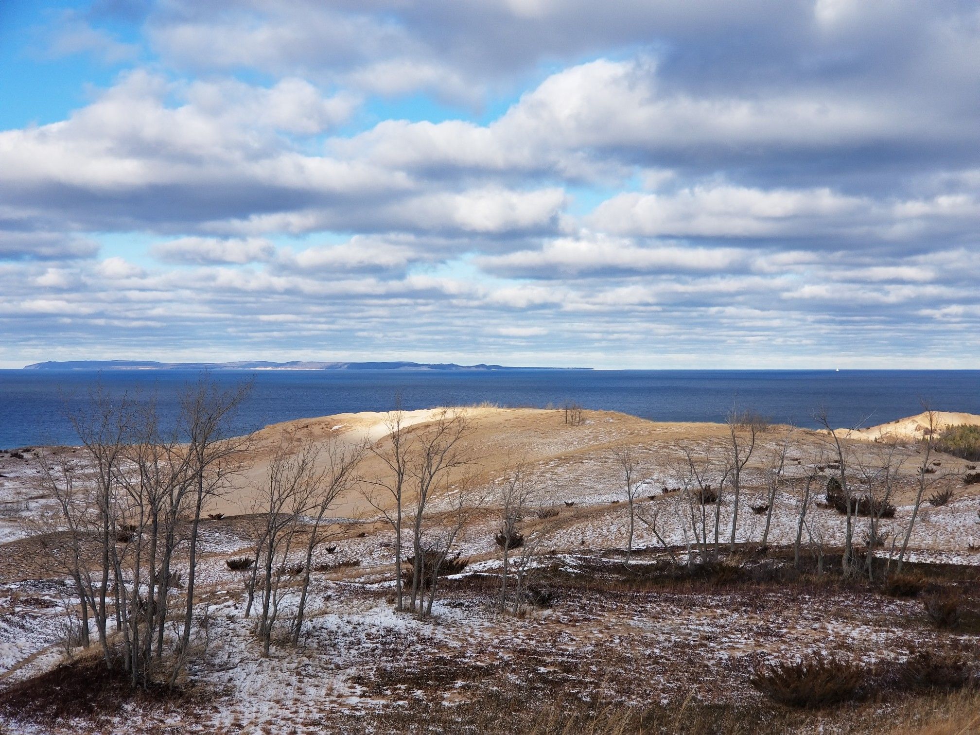 Snowy dunes and bare trees overlook a vast blue lake under cloudy sky. - Dune Climb and Sleeping Bear Point Loop