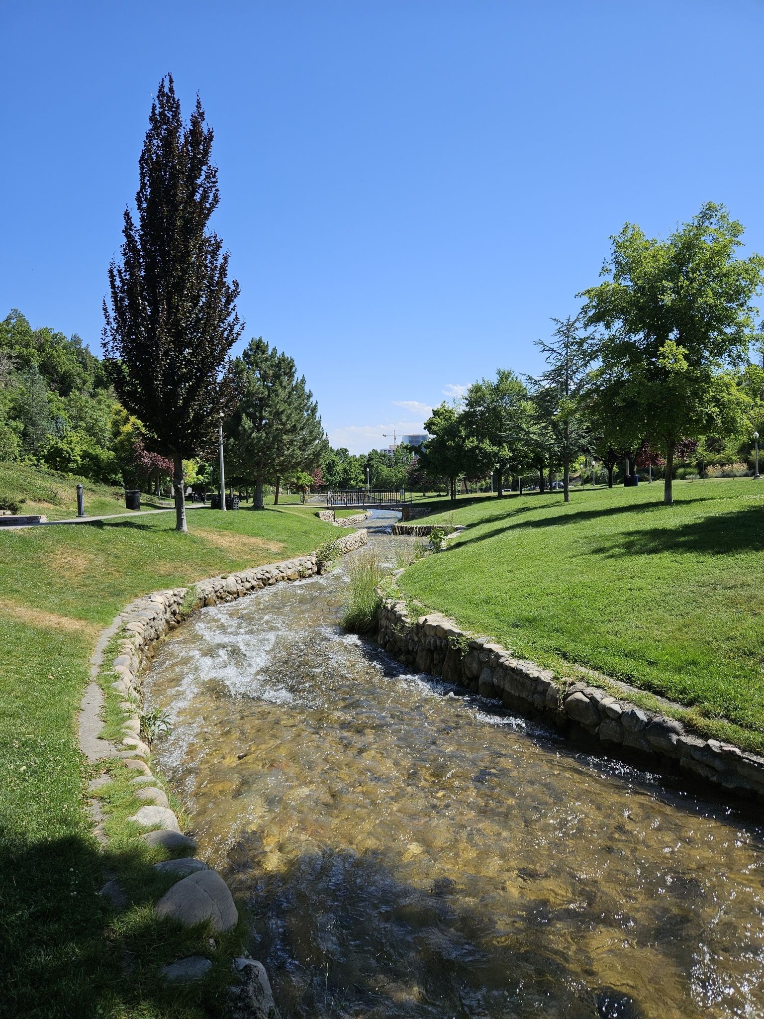 A clear stream flows through a lush green park on a bright sunny day. - Memory Grove Park – Mormon Battalion Monument loop from Salt Lake City