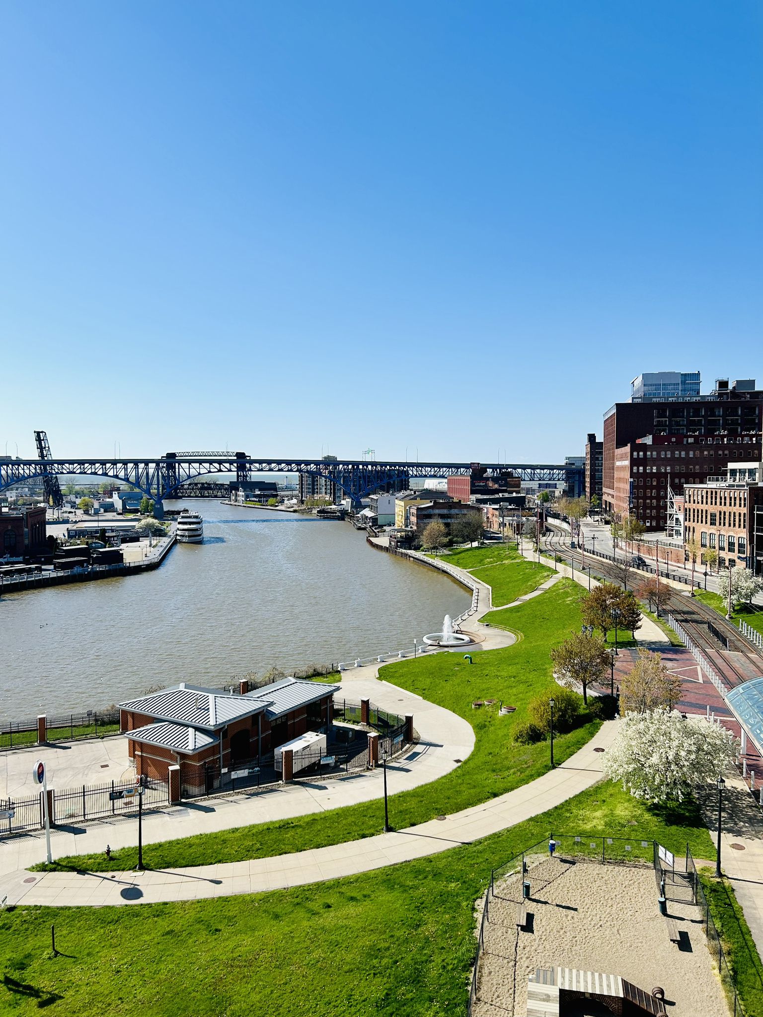 River flowing through a city park with paths, buildings, and a distant bridge. - Cleveland Lakefront Bikeway