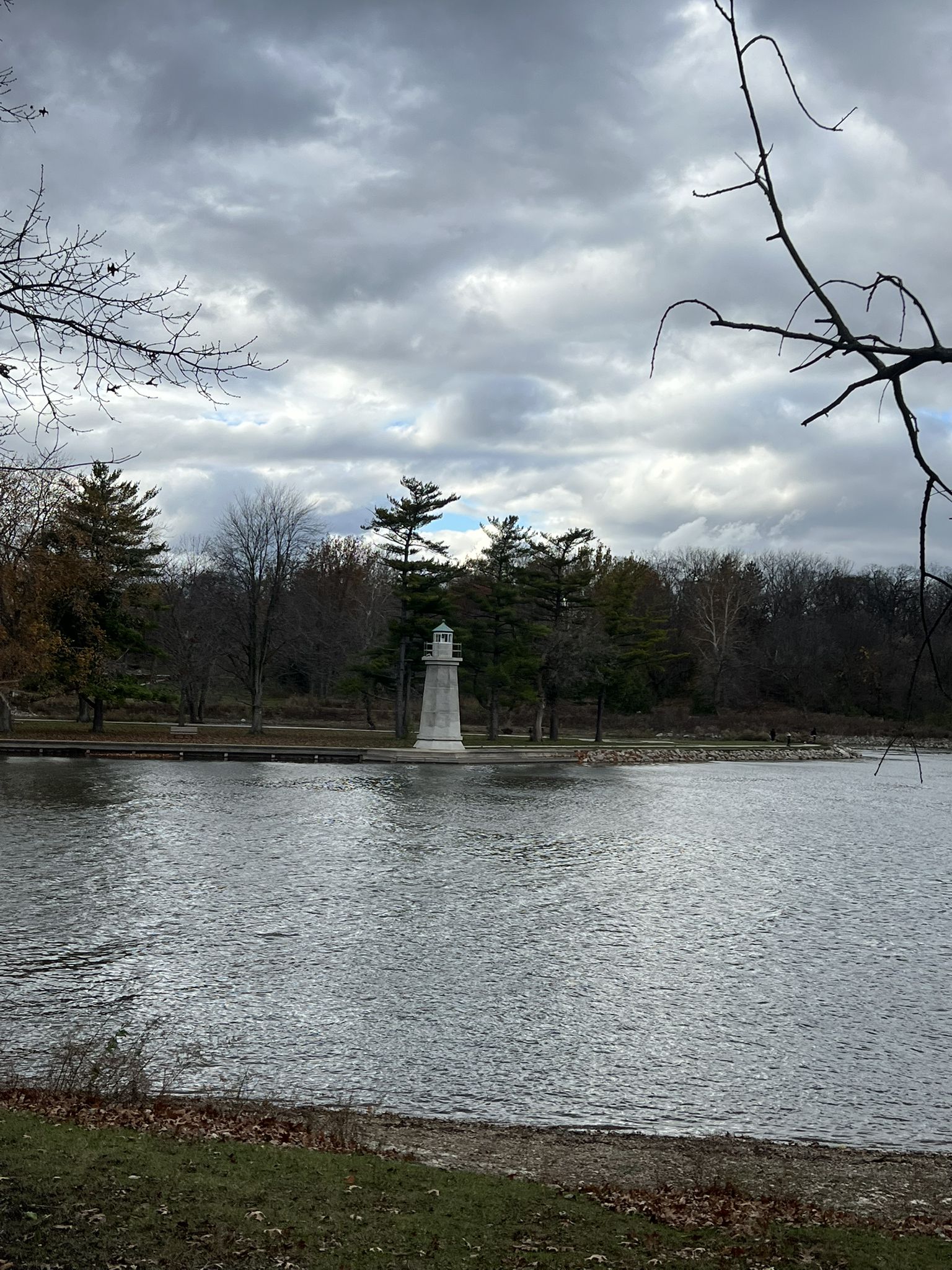 A white lighthouse stands in a lake under a dramatic, cloudy sky. - Fabyan Forest Preserve – View of Fabyan Windmill loop from North Aurora