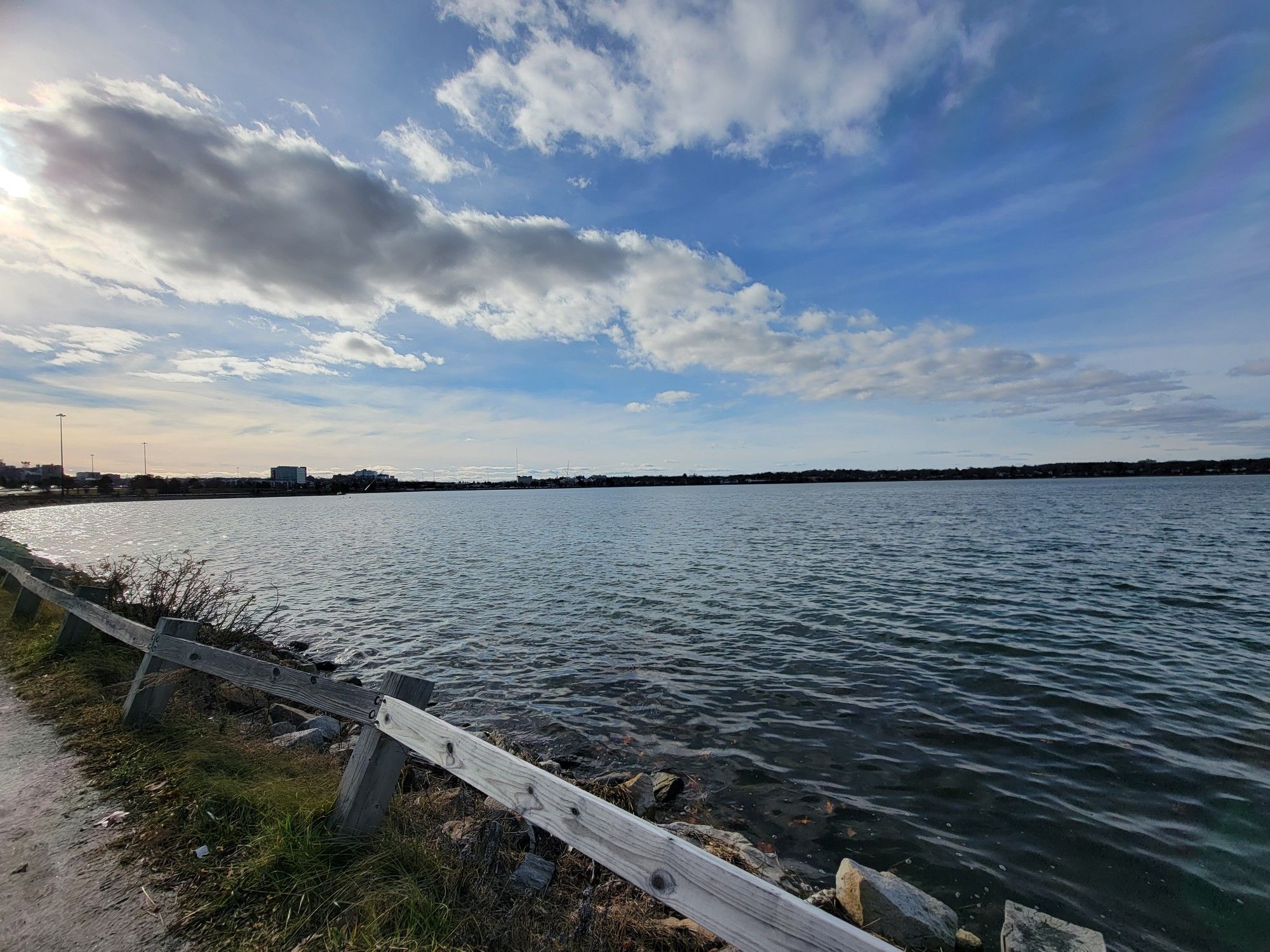 A wide view of a lake with a wooden fence along the shore under a cloudy sky. - Back Cove Trail