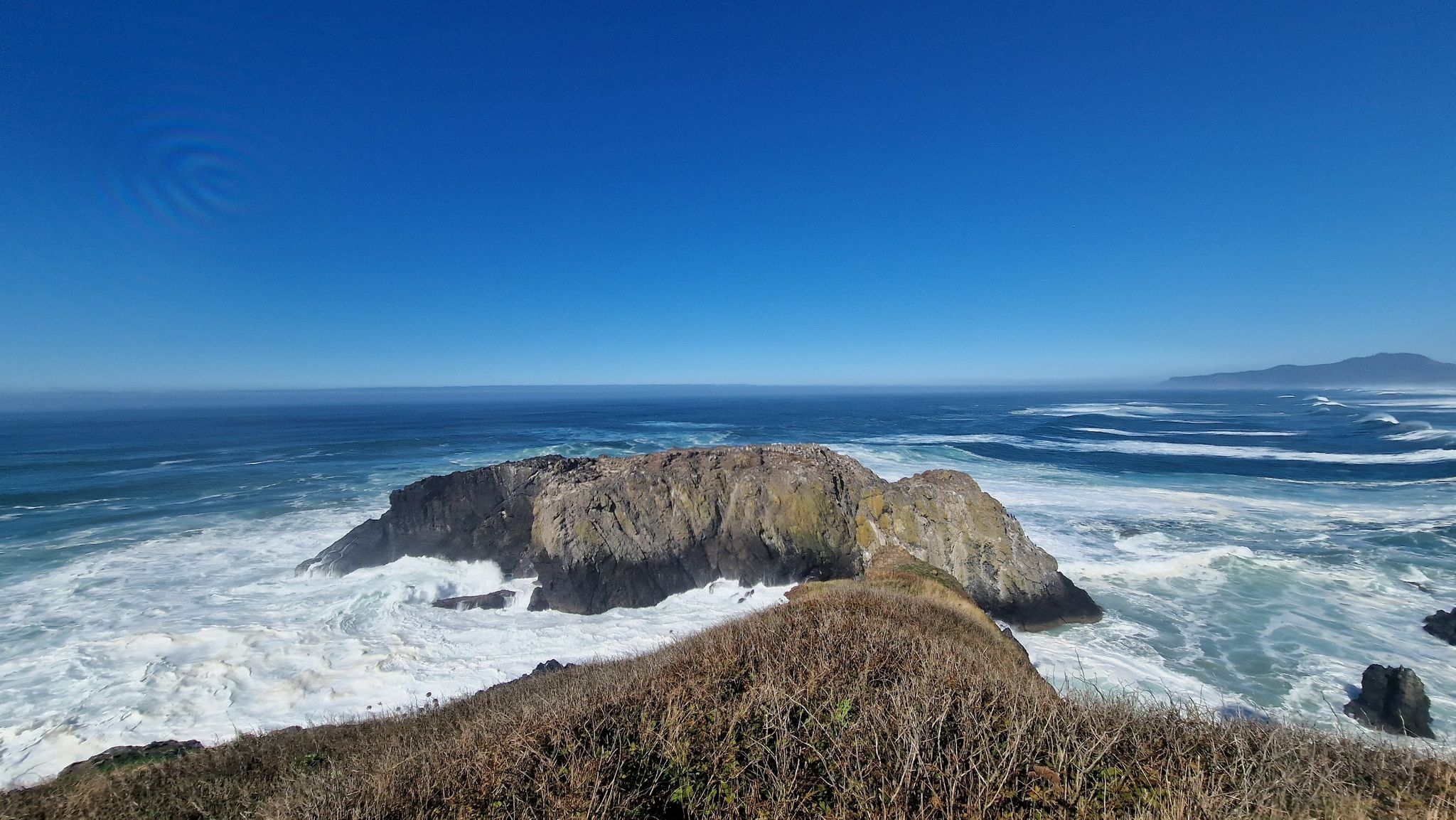 Panoramic ocean view with a large rocky island, crashing waves, and clear sky. - Salal Hill and Lighthouse Trail