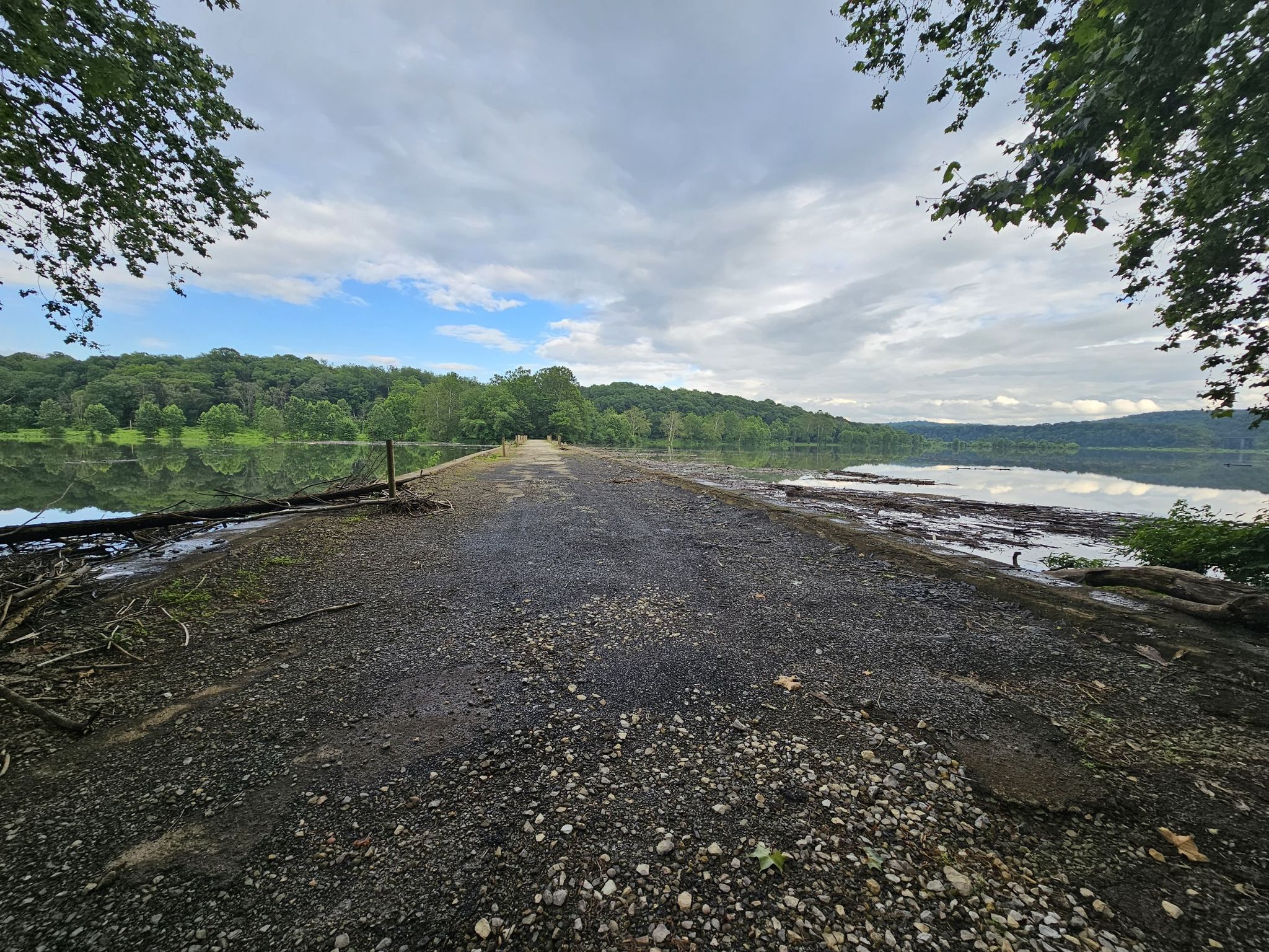 Gravel path extending into a calm lake, surrounded by green trees. - West Penn Trail