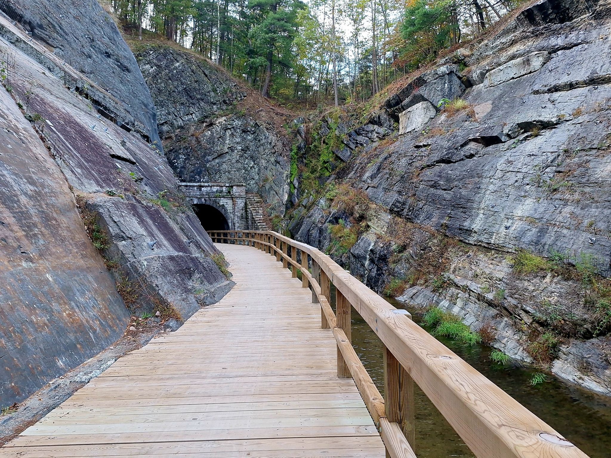Wooden boardwalk curves towards a stone tunnel entrance in a rocky gorge. - Chesapeake and Ohio Canal Towpath