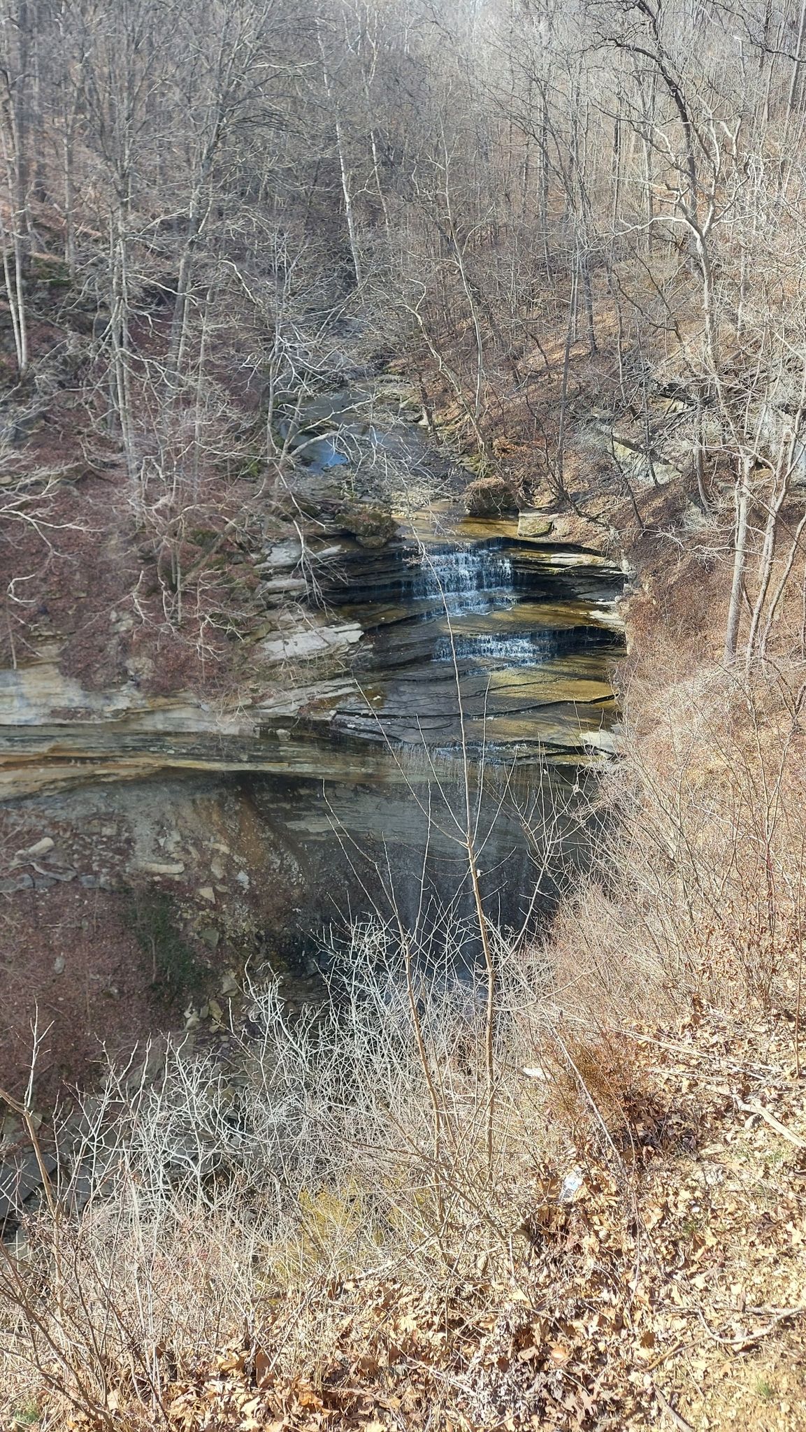 A small waterfall cascades over a rocky cliff surrounded by bare trees. - Trail 7