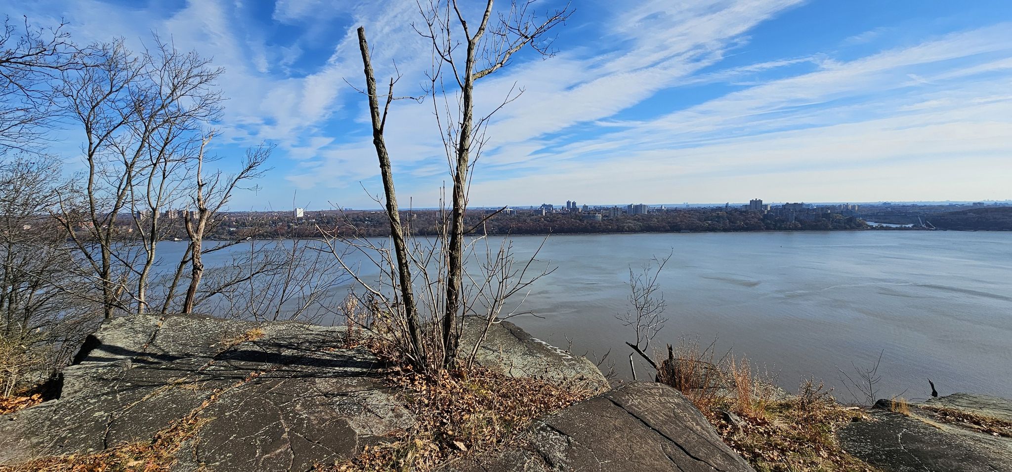Wide river view from rocky cliff with bare trees and distant city under bright sky. - Long Path and Shore Trail Loop