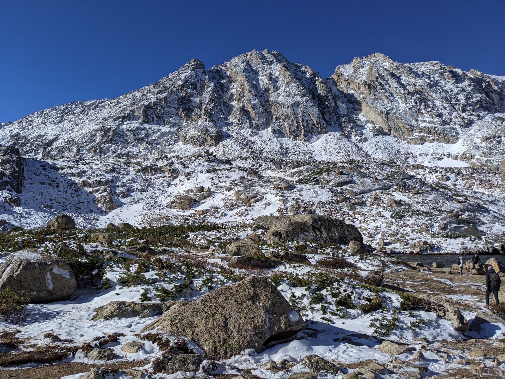 Brightly lit, snow-dusted mountains with a person walking in the rocky foreground. - Blue Lake via Mitchell Lake Trail