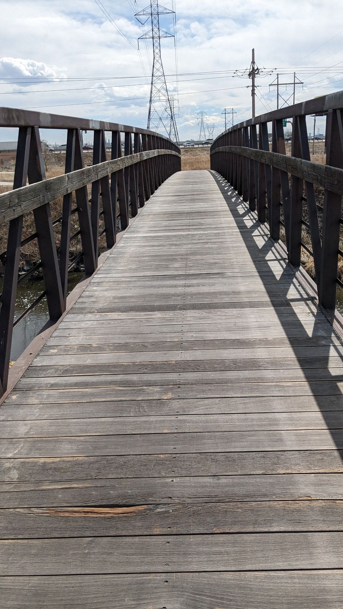 Curved wooden pedestrian bridge stretching over a dry, open landscape. - South Platte River – Sand Creek Regional Greenway loop from Dick's Sporting Goods Park