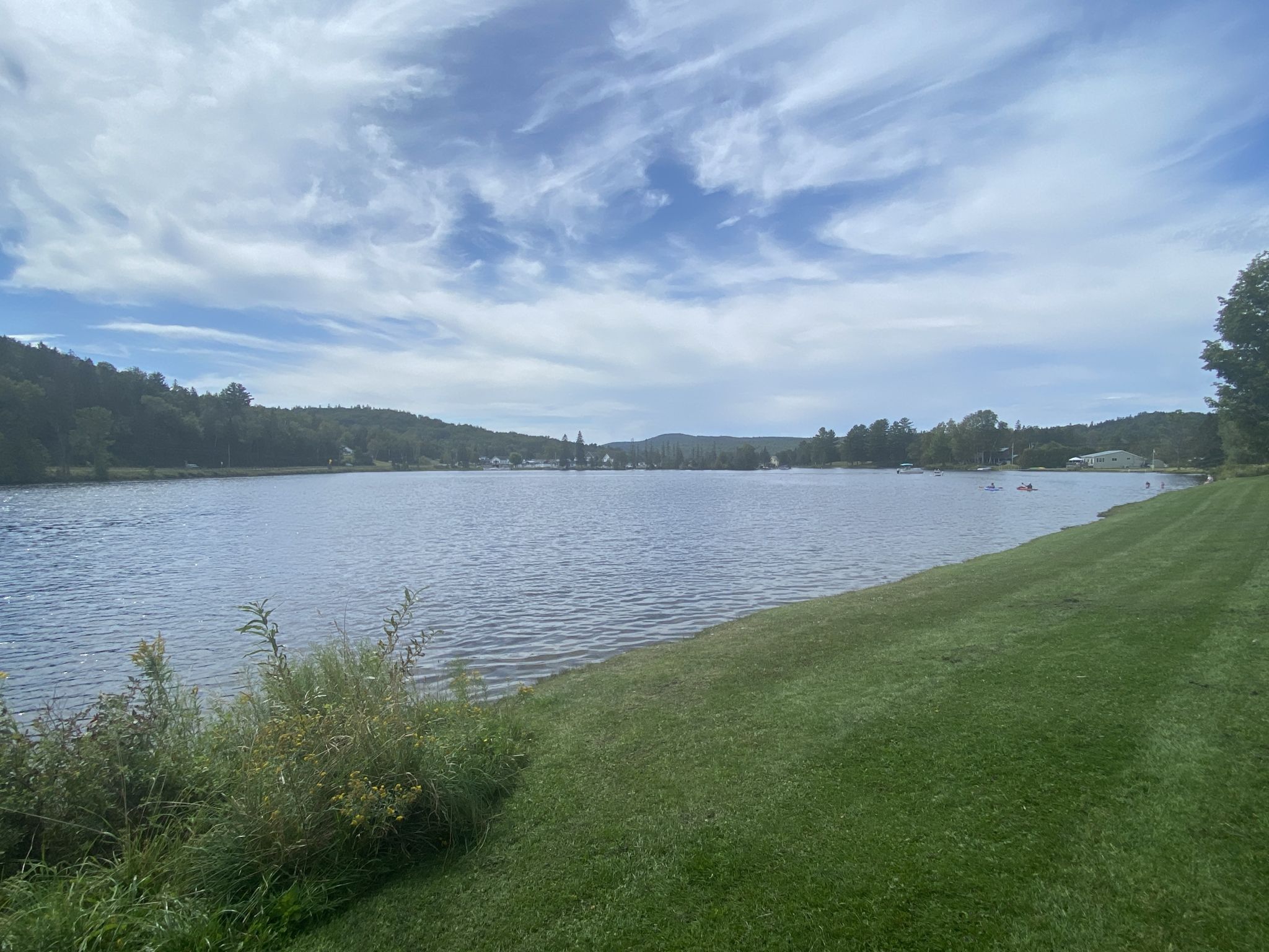 A wide lake with green grassy shore, distant hills, and a partly cloudy sky. - Wonderful Lamoille Rail Trail – Public Access Tools and Pump loop from Goodfellas