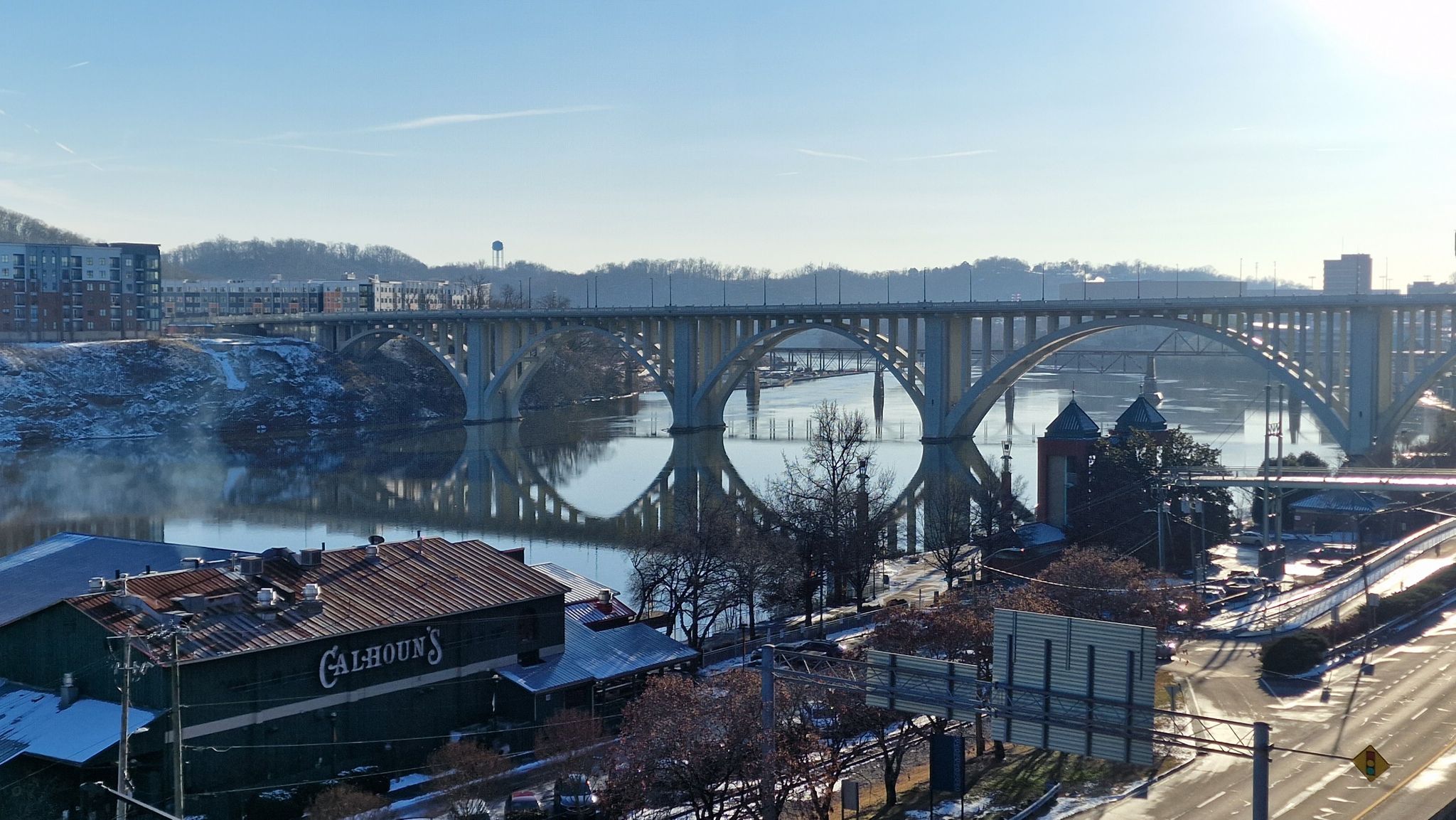A large arched bridge spans a wide river with city buildings and snow. - South Knoxville loop
