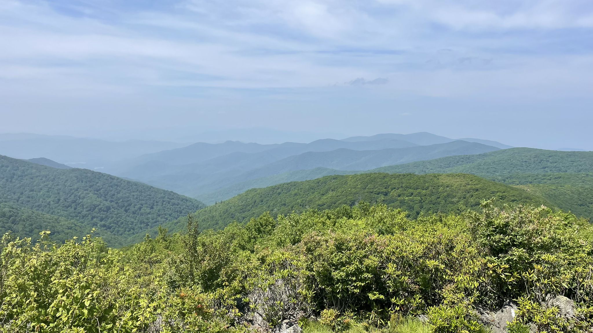 Expansive view of green, hazy mountain ranges under a light blue sky. - Rocky Top via Anthony Creek Trail