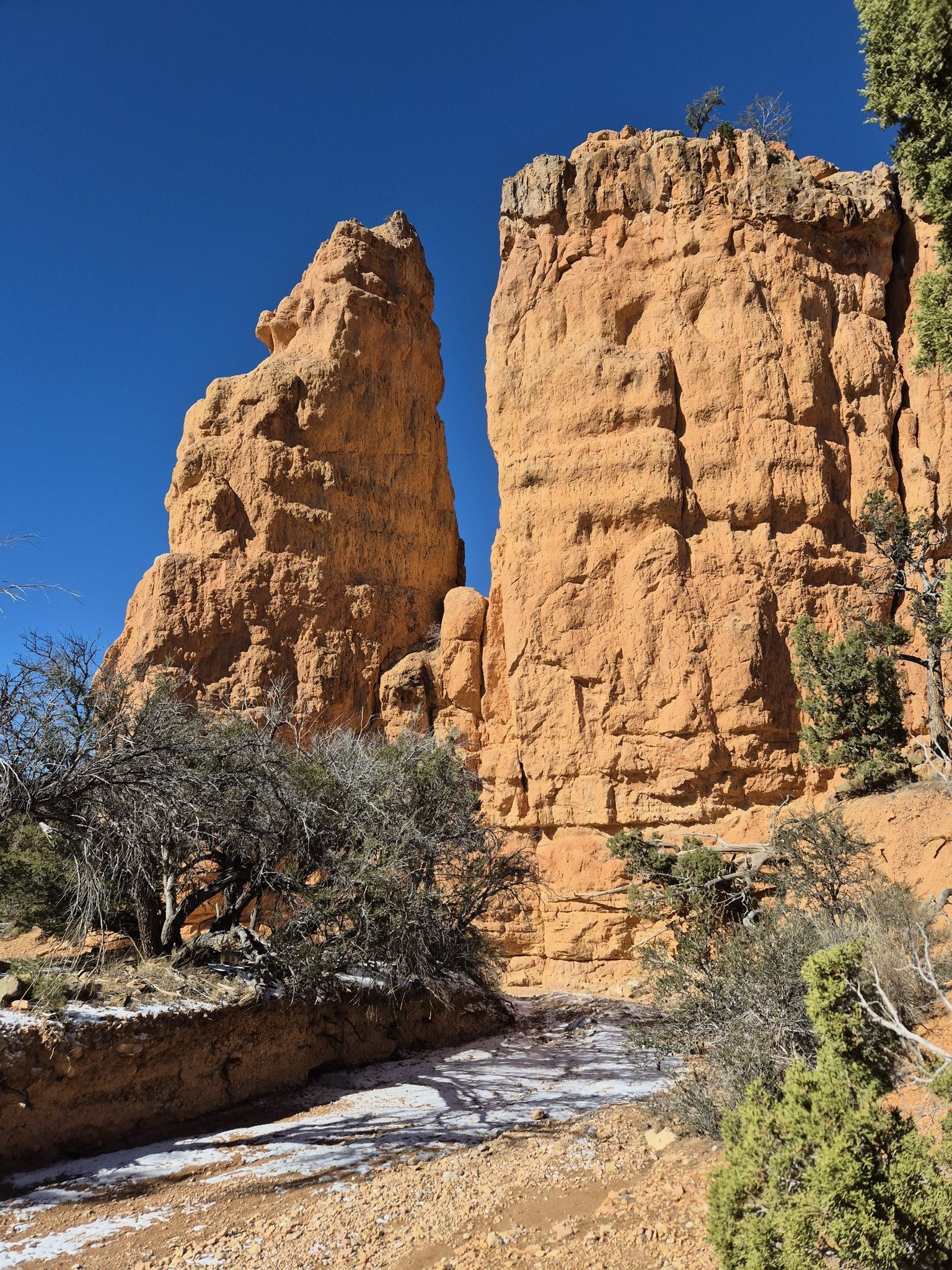 Two towering red rock formations flank a snowy path under a clear blue sky. - Hiking loop from Black Mountain