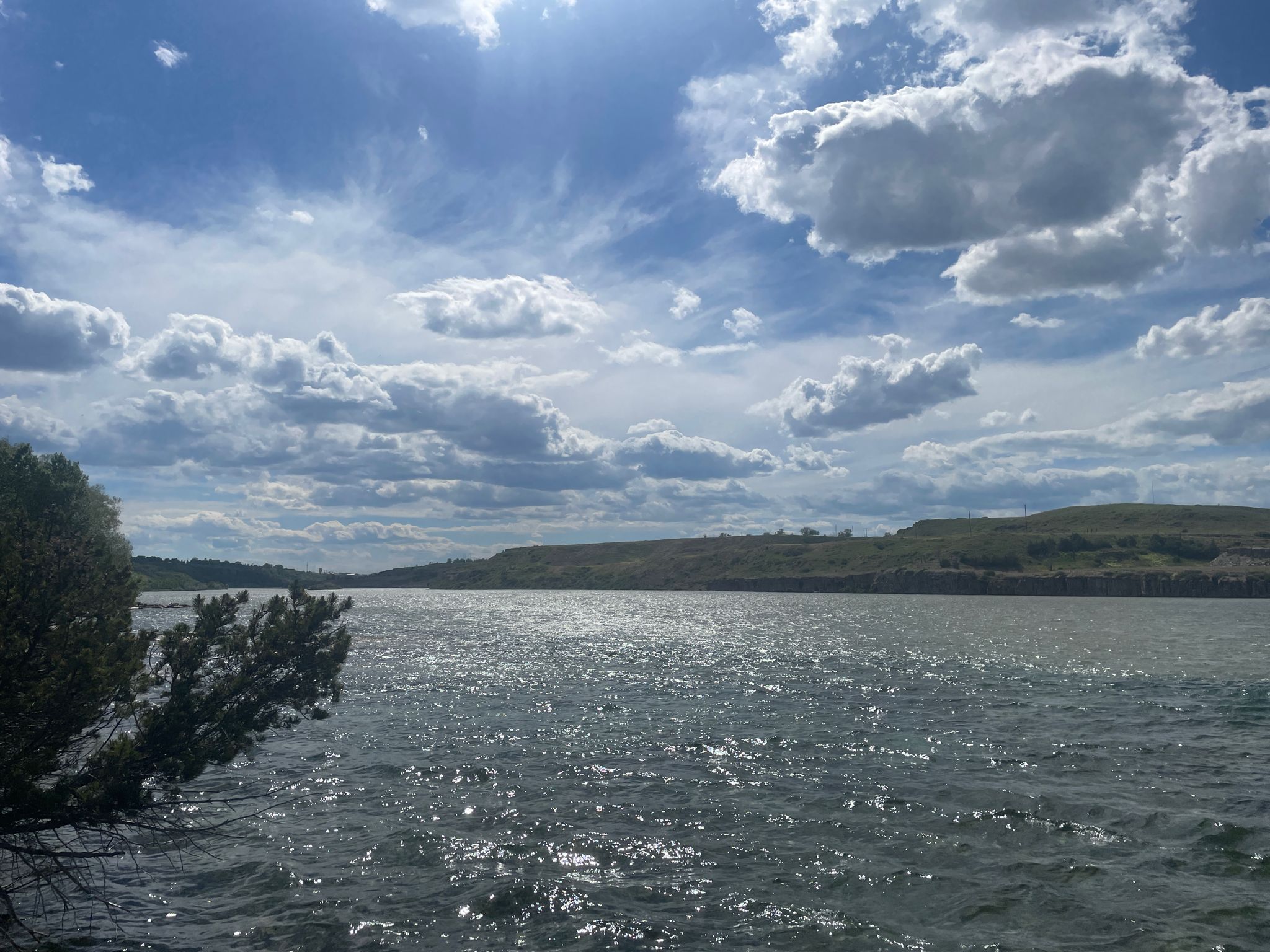 Bright sun over a wide lake with distant hills and cloudy sky. - River's Edge Trail