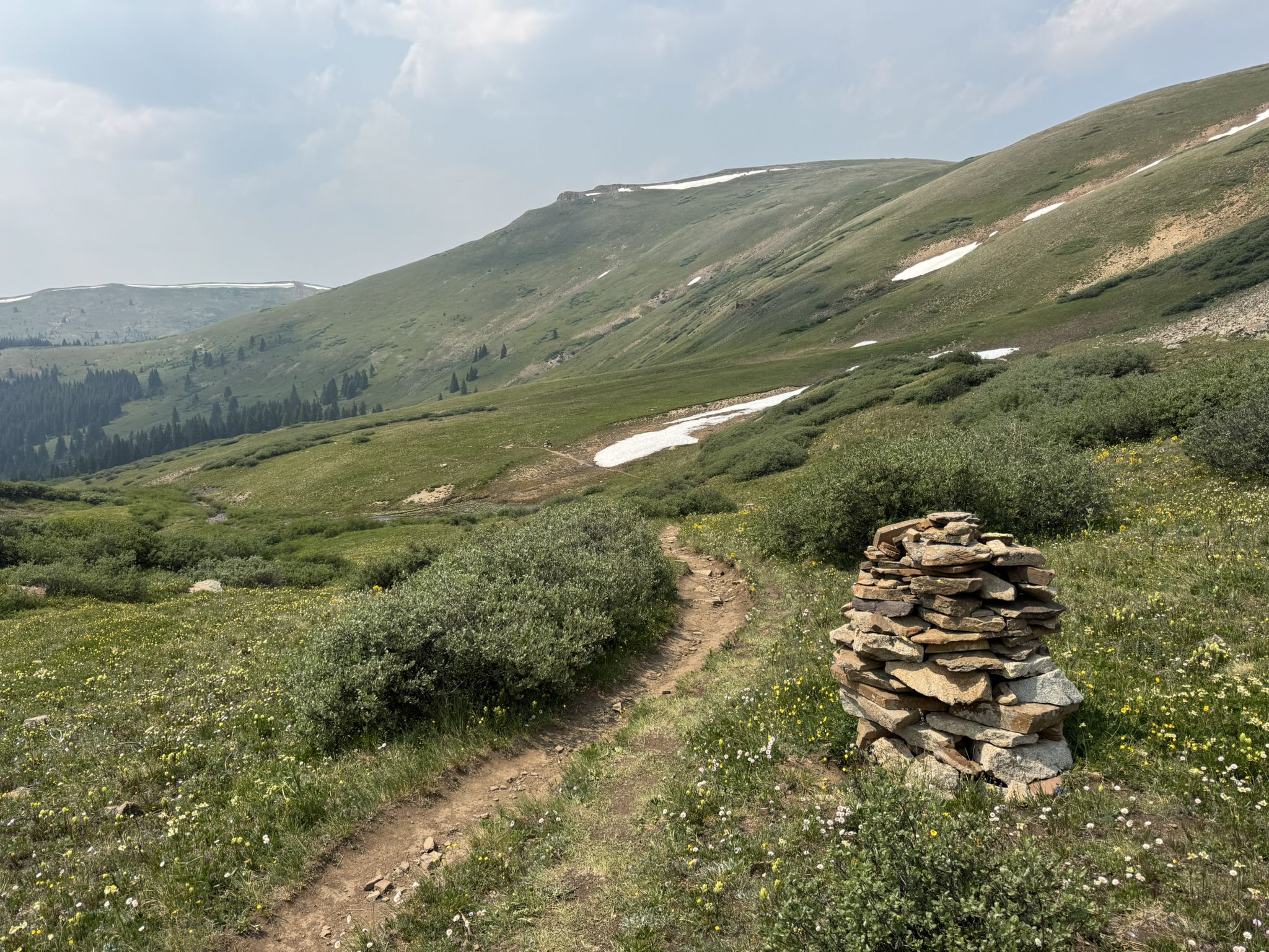 A rock cairn beside a dirt path on a green, grassy mountain slope. - Colorado Trail: Camp Hale to Kokomo Pass