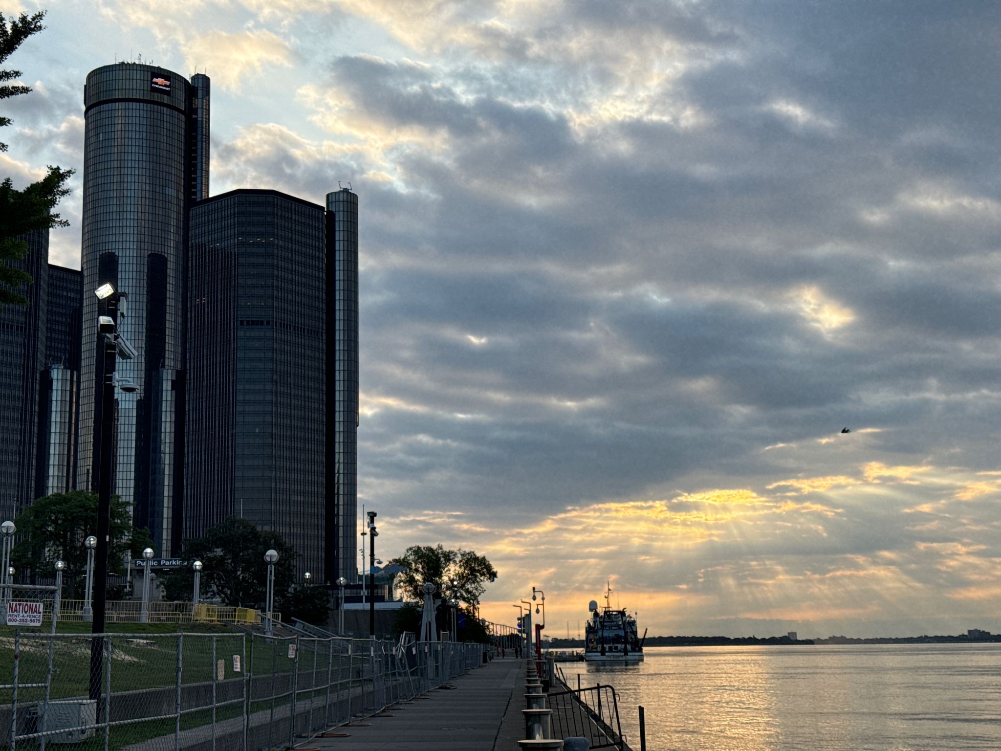 Tall city buildings beside a river at sunset with dramatic cloudy sky. - Detroit Riverwalk and Dequindre Cut Loop