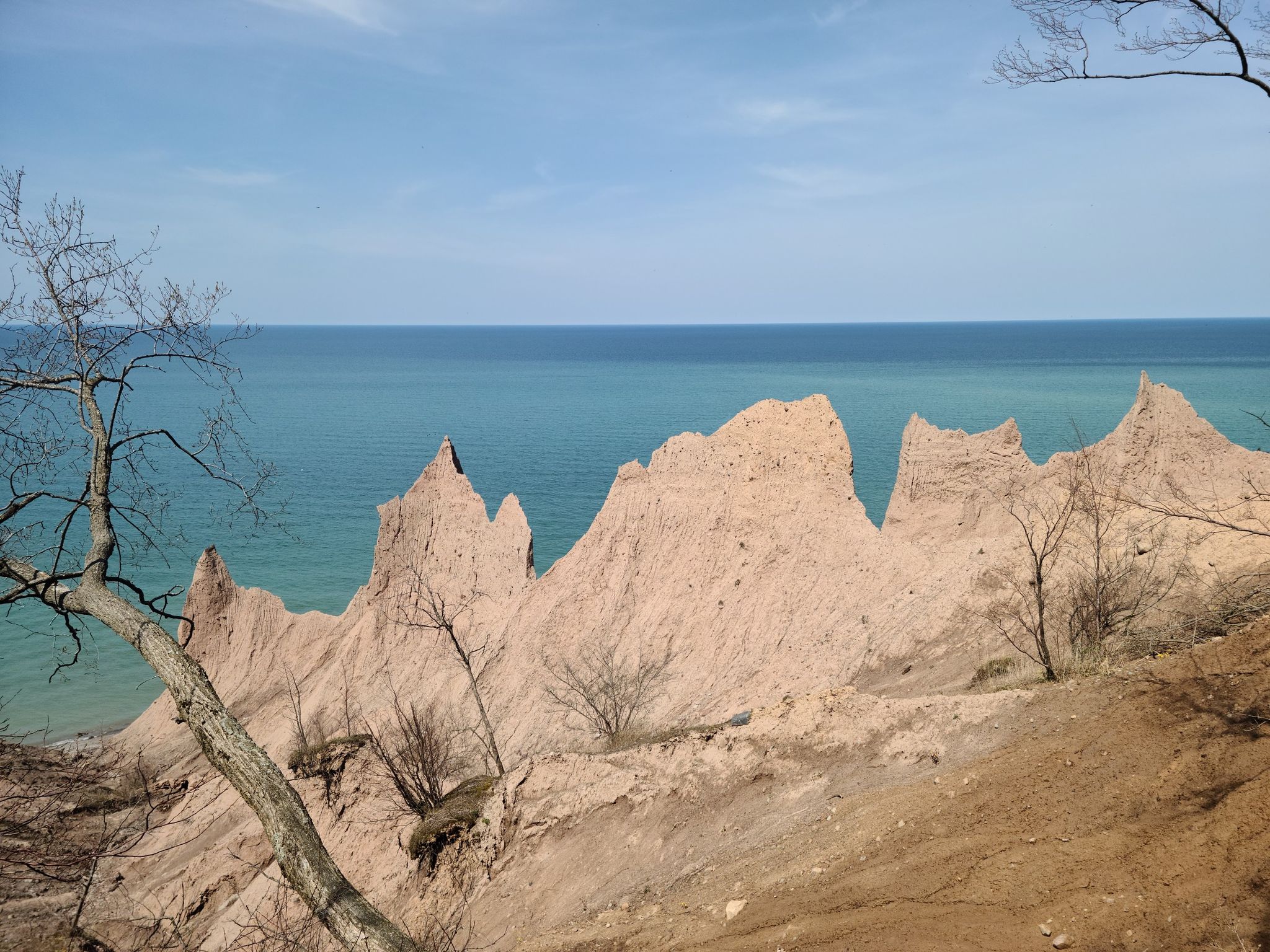 Eroded sandy cliffs meet a calm blue sea under a bright sky. - Chimney Bluffs – Chimney Bluffs loop from Chimney Bluffs State Park