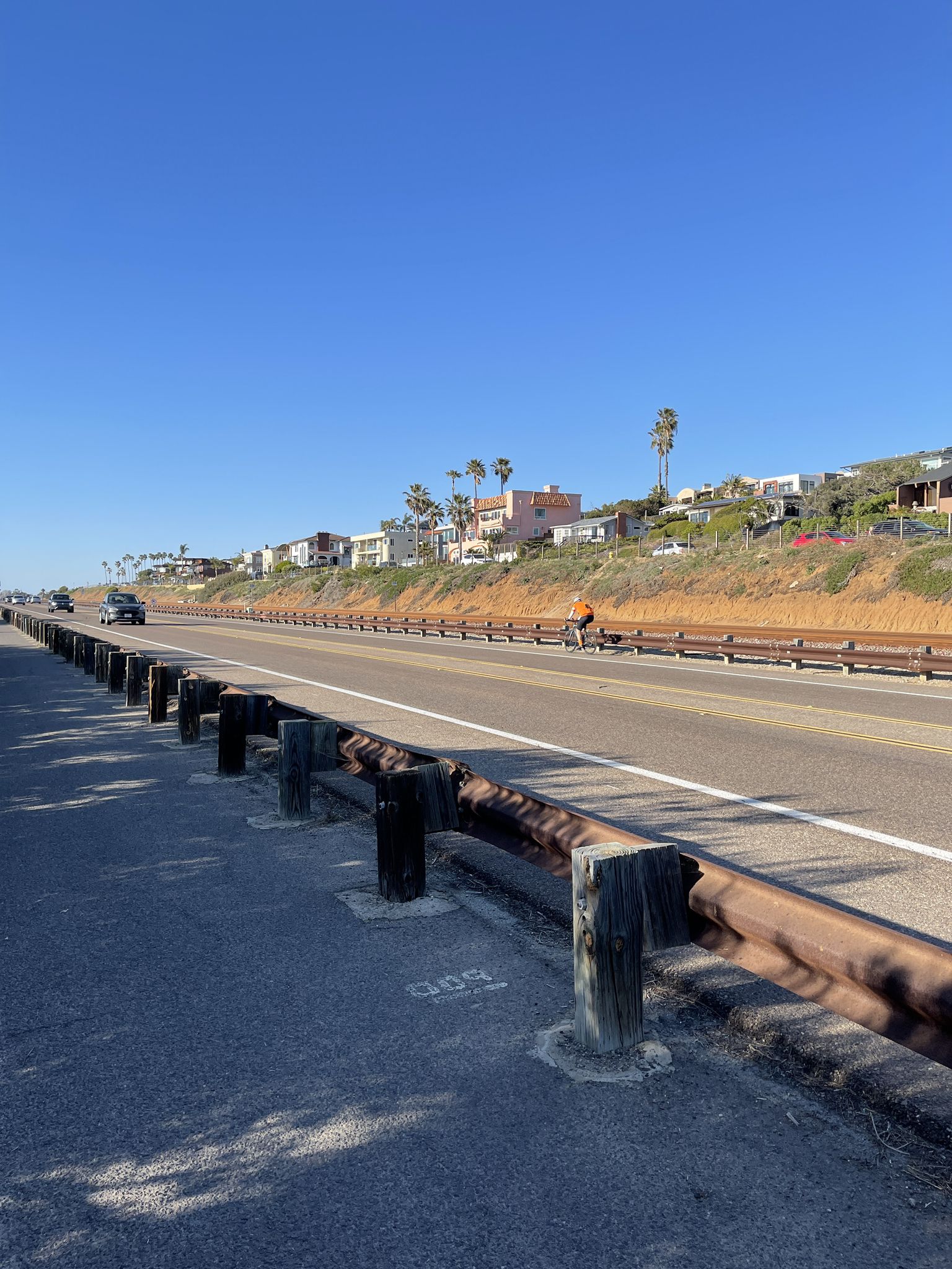 Bright highway with guardrail, cars, and hillside houses under clear sky. - San Elijo Lagoon Estuary Canal – Swami's Seaside Park loop from Hunter 1940 Parking Lot