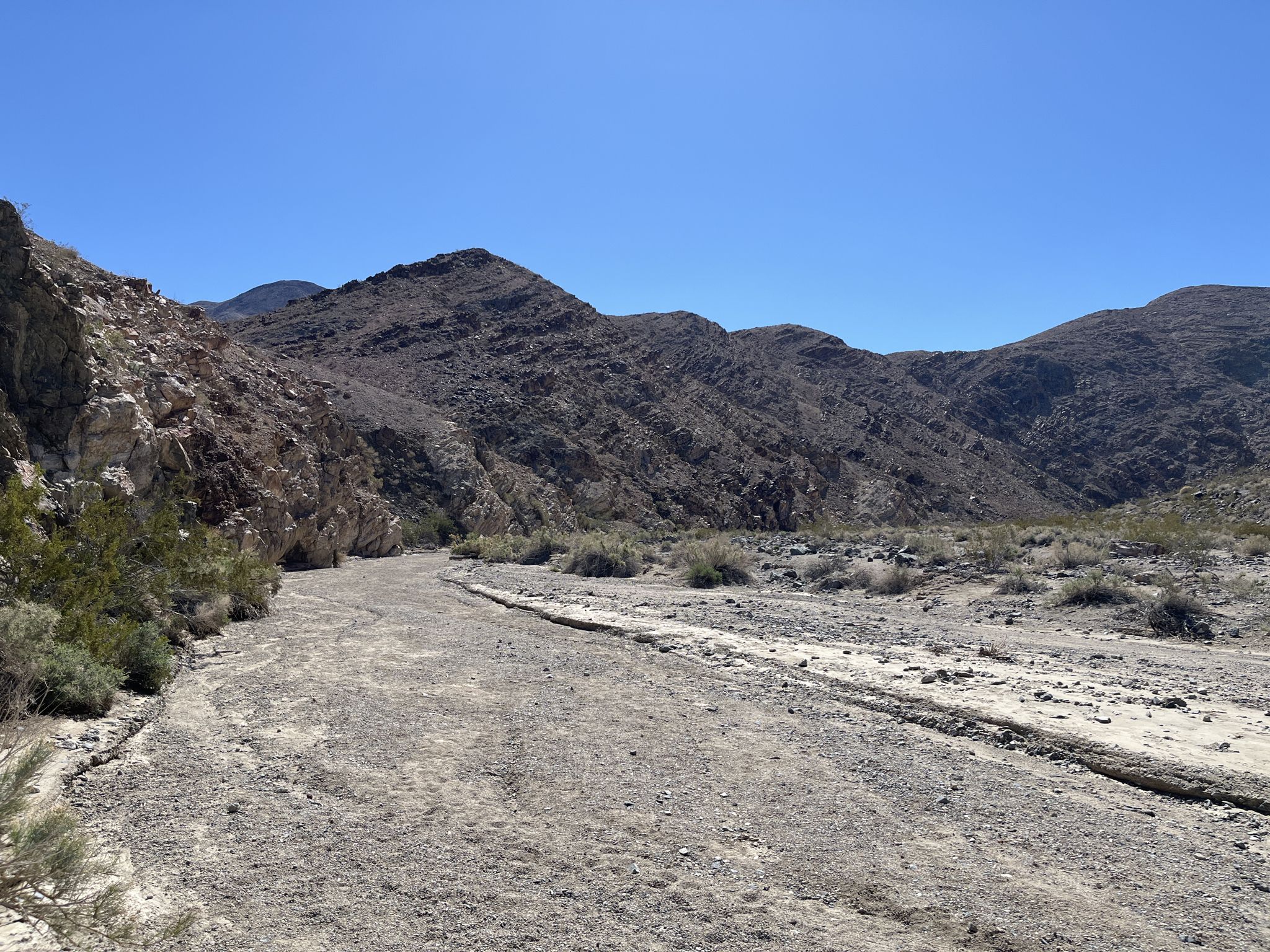 A wide, dry desert wash leads into rocky mountains under a clear sky. - Darwin Falls Trail – Darwin Falls loop from Panamint Springs