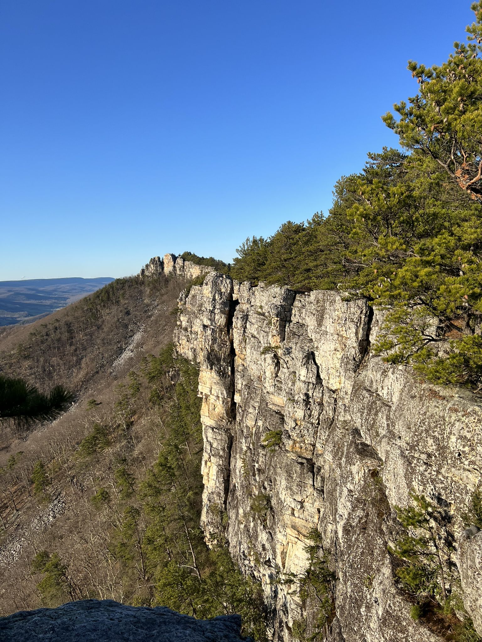 Dramatic rock cliff face beside a forested mountain ridge under clear skies. - North Fork loop