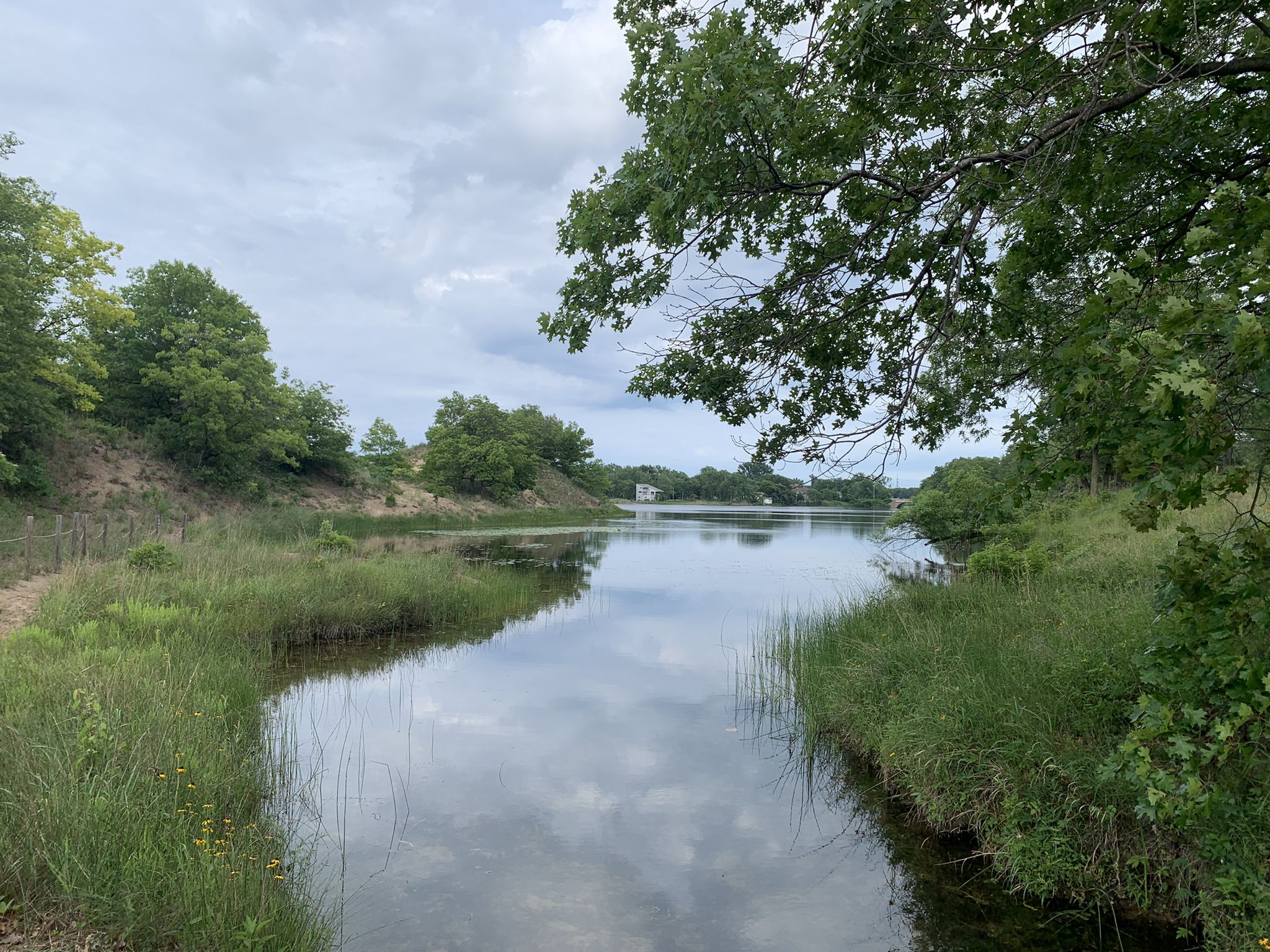 A narrow waterway with green banks under a cloudy sky, surrounded by trees. - Paul H. Douglas Trail