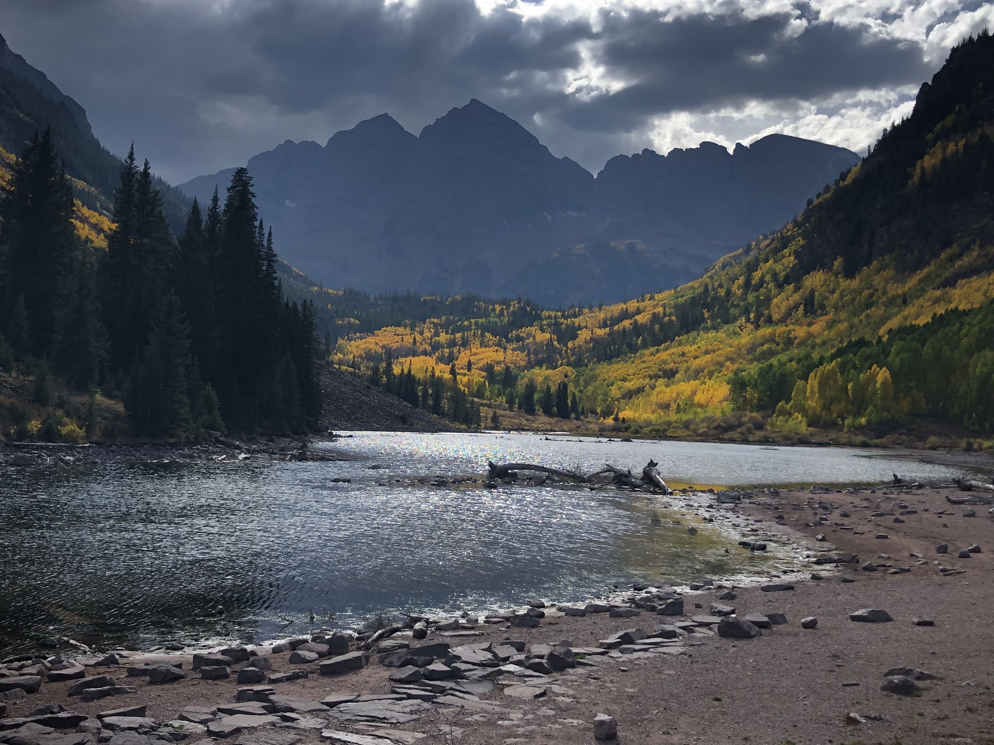 Dark lake reflecting dramatic mountains and golden autumn trees under cloudy sky. - Buckskin Pass