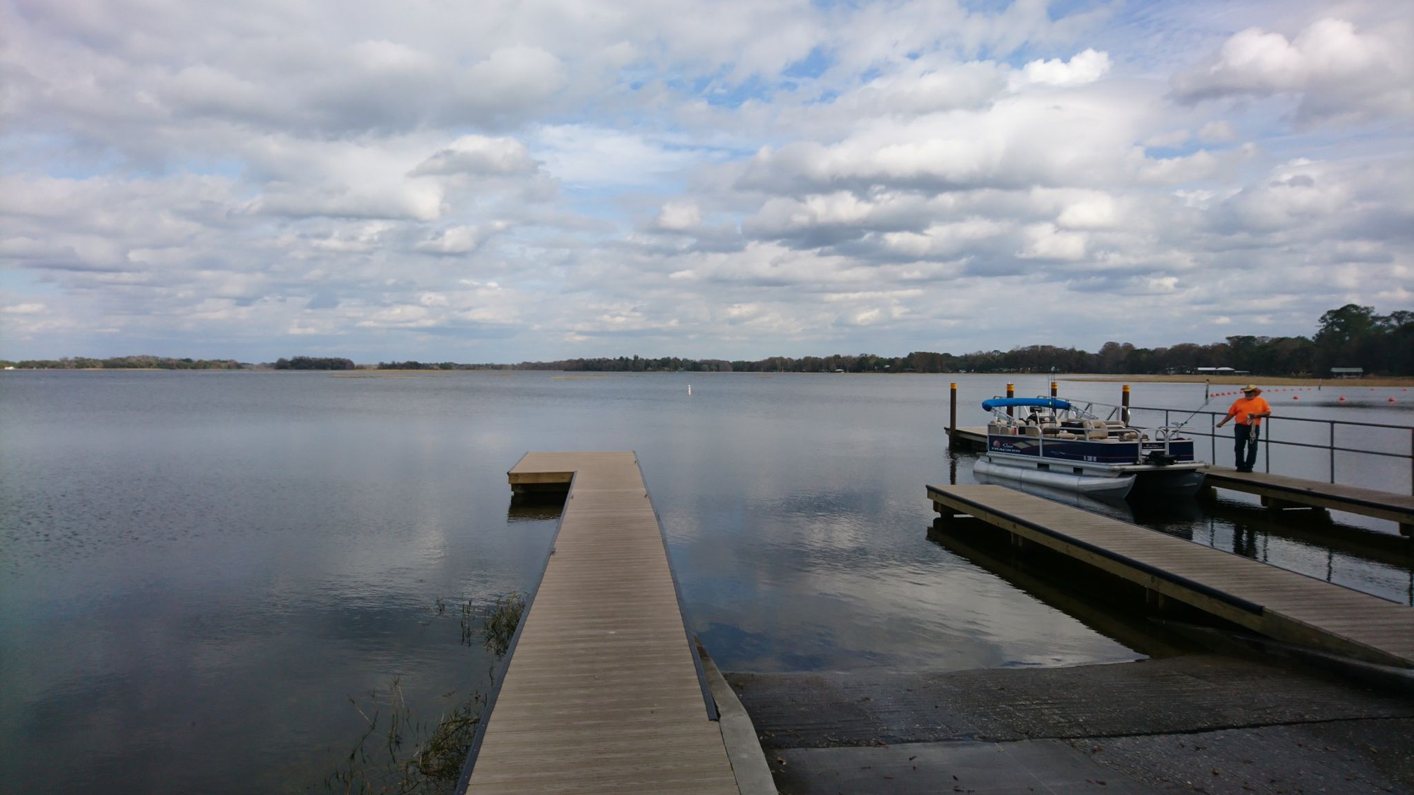 Overcast day at a wide lake with docks, a boat, and a person. - Withlacoochee State Trail