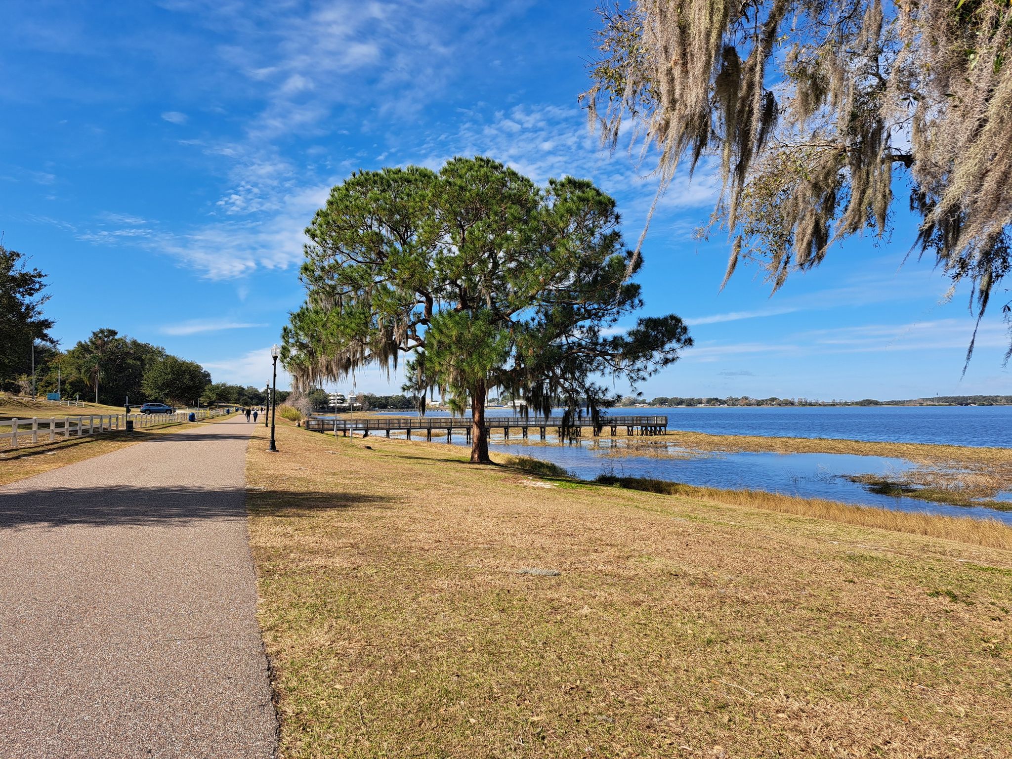 Paved path next to a lake with a pier and large trees. - Epic Cycles – Lake Hiawatha Preserve loop from Clermont