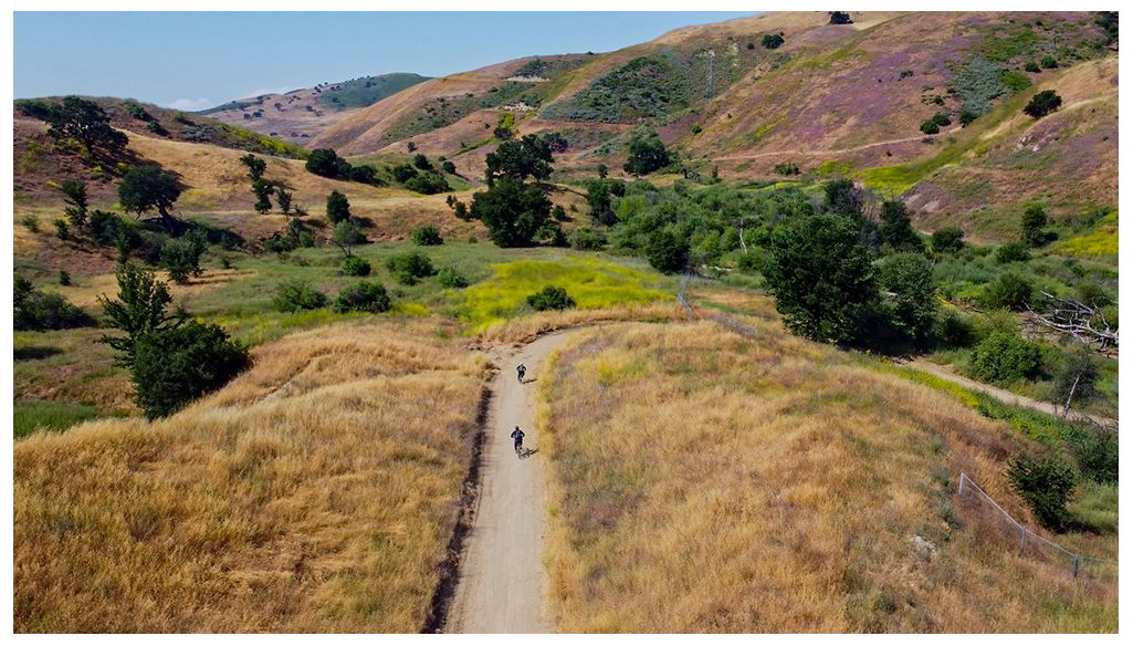 Two people cycle on a dirt path through golden hills and green trees. - Ahmanson Ranch House and Mary Wiesbrock Loop Trail