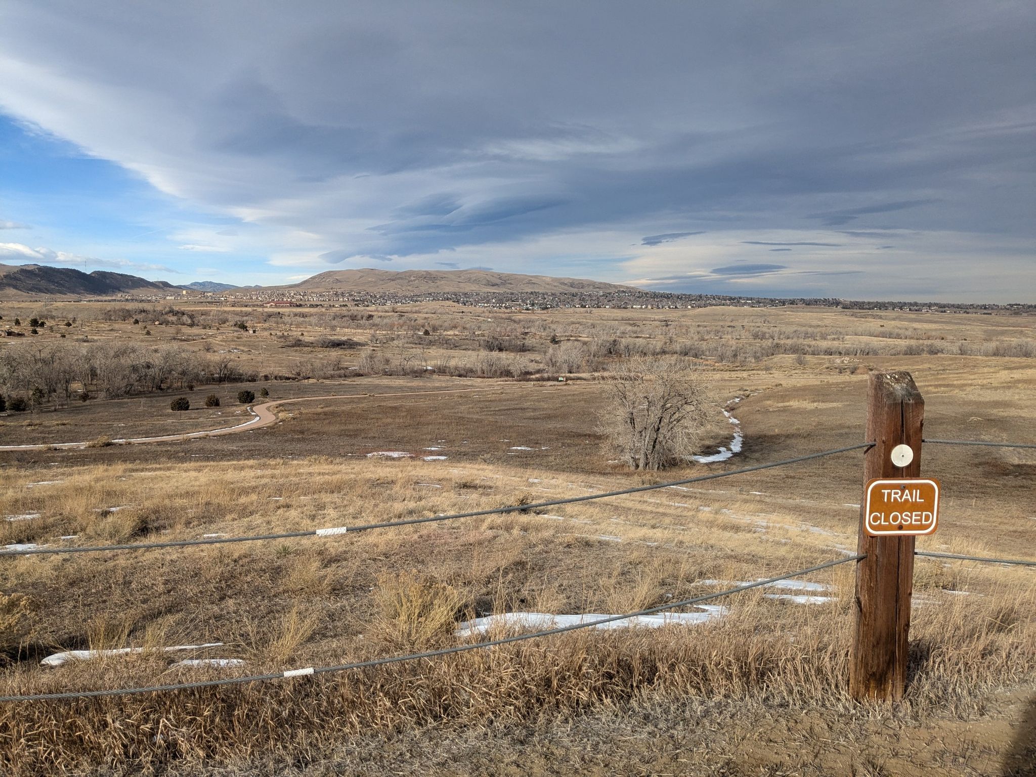 A 'Trail Closed' sign in a vast, dry, hilly landscape under a cloudy sky. - View of Harriman Lake loop from Federal Correctional Institution, Englewood