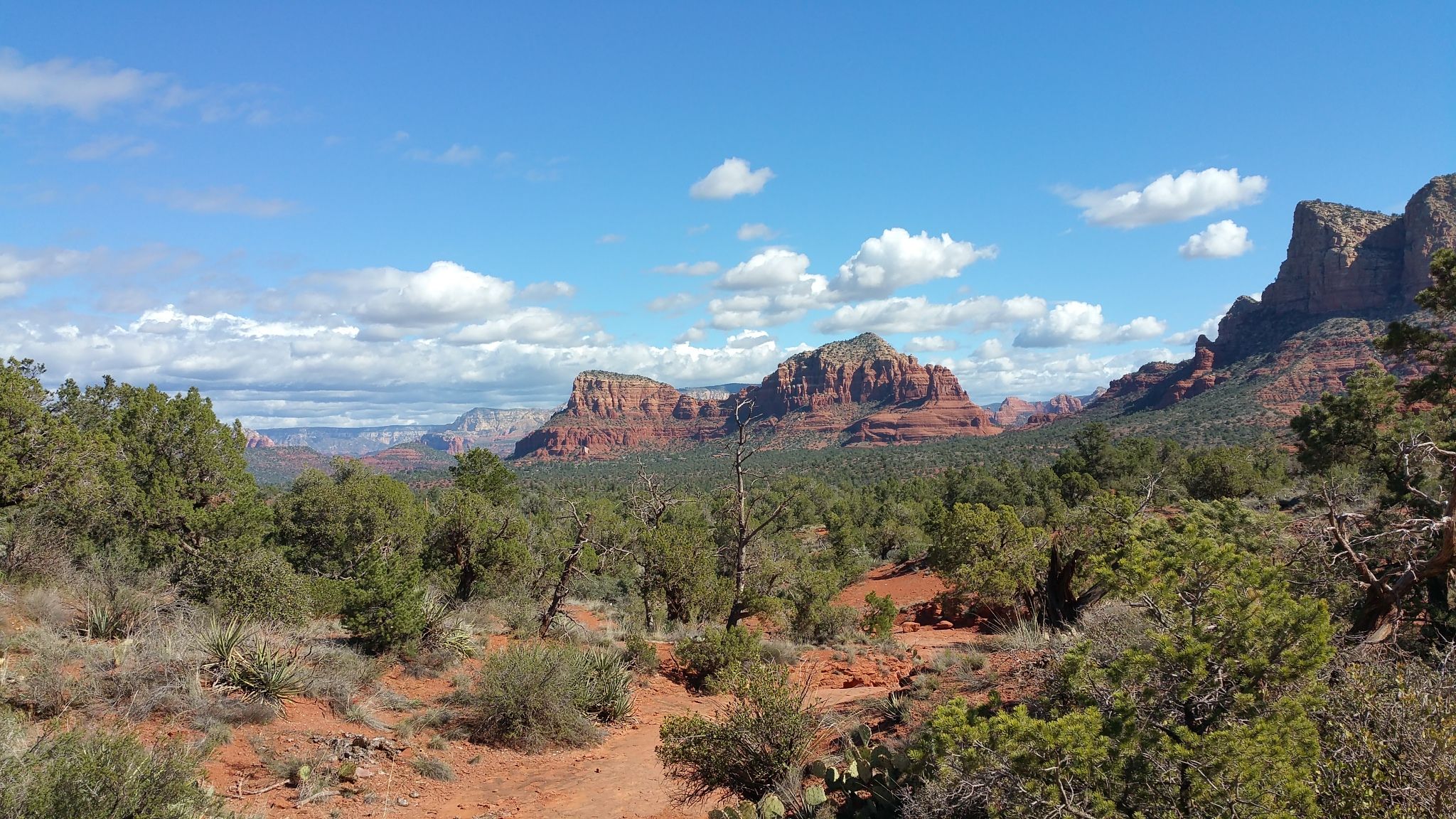 Panoramic view of red rock mountains and green desert under a cloudy blue sky. - Courthouse Butte and Bell Rock Loop
