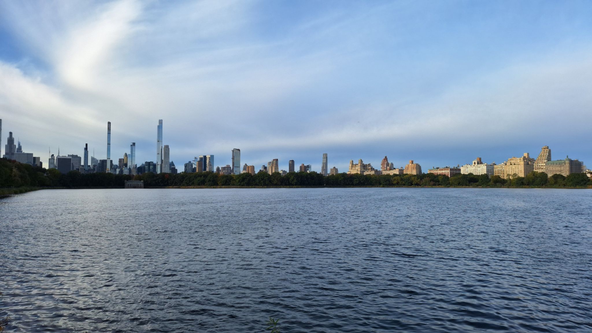 Wide lake with a distant city skyline under a dramatic cloudy sky. - Bow Bridge, Central Park – Central Park loop from Grand Central–42nd Street