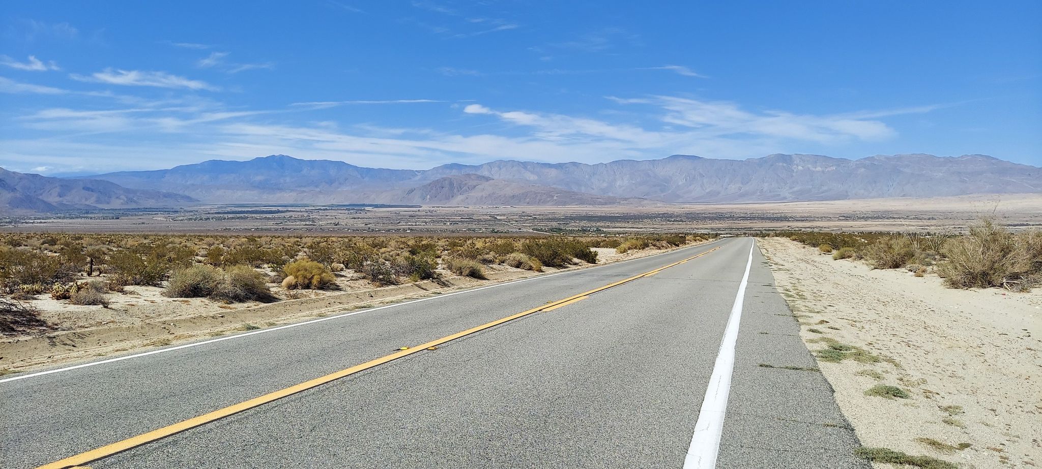 Long straight desert road stretching towards distant mountains under a blue sky. - Desert Eagle Sculpture – Yaqui Pass loop from Borrego Springs