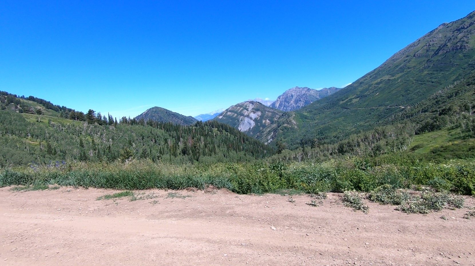 Dirt road in foreground, leading to lush green mountains and rocky peaks. - Kyhv Peak Road