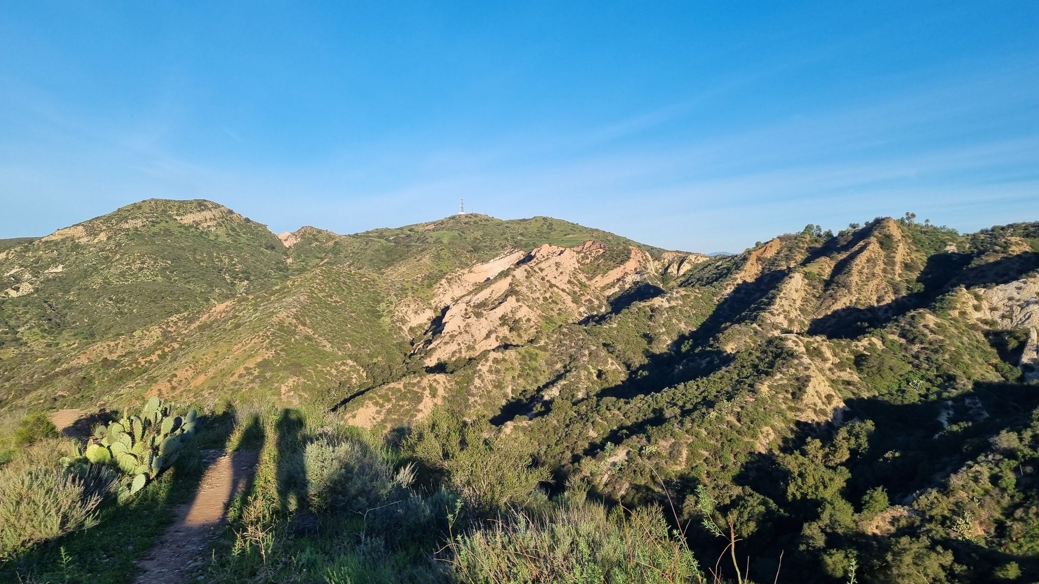 Shadows of people on a sunlit mountain trail with rocky peaks. - Borrego Trail and Billy Goat Loop